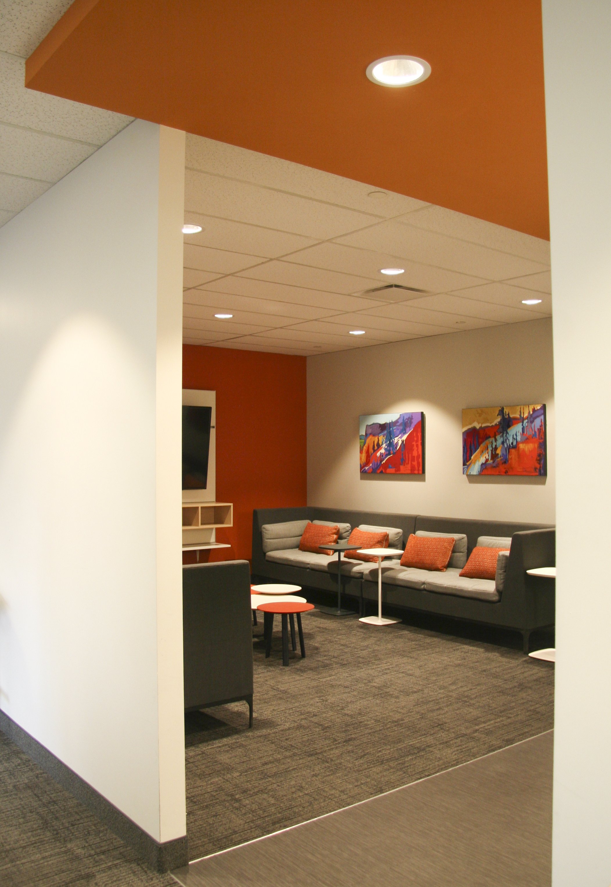 Modern lounge area with gray sofas, orange cushions, abstract wall art, and small round tables.