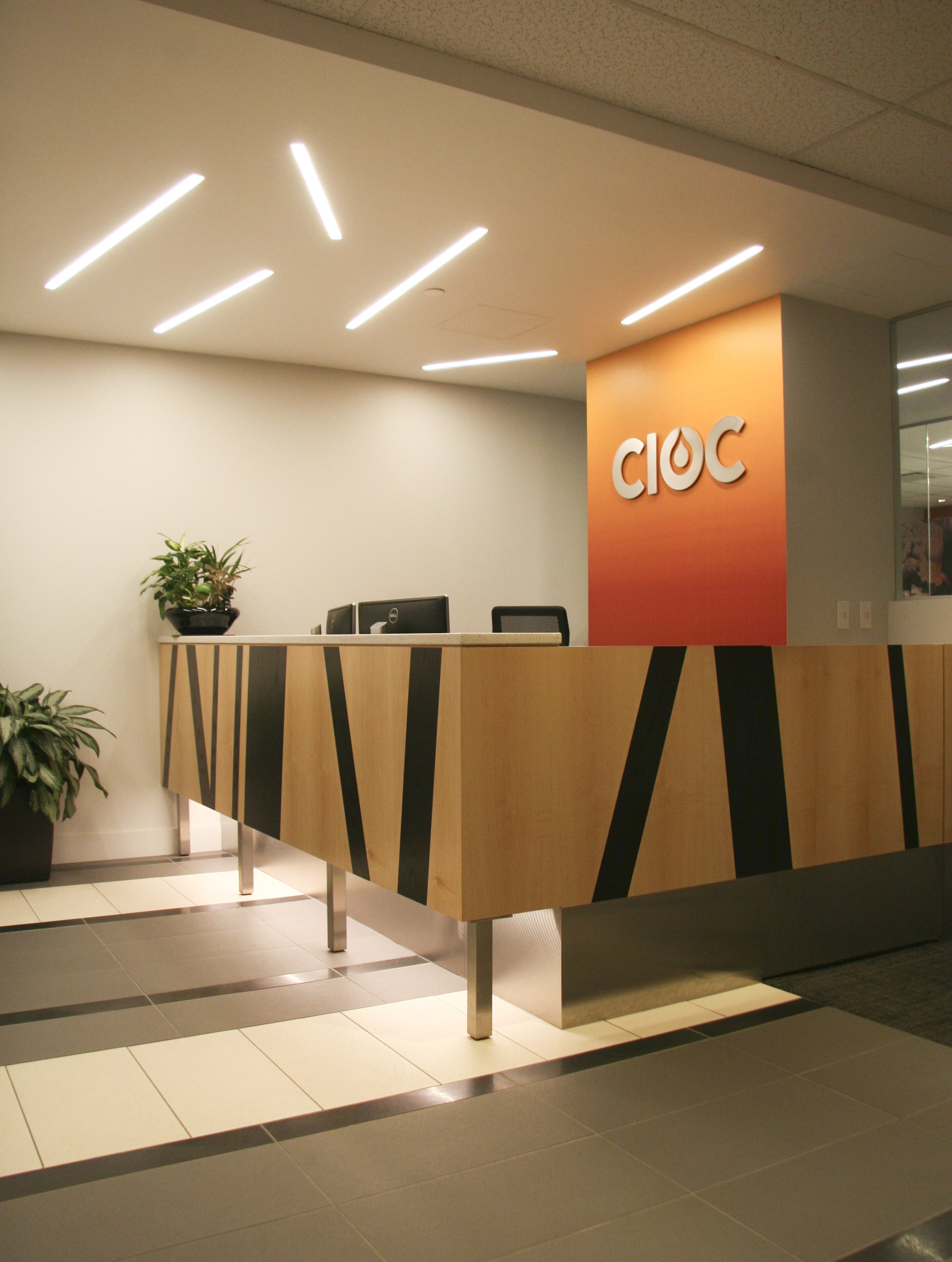 Modern office reception area with geometric desk and the letters 'CIOC' on an orange wall.