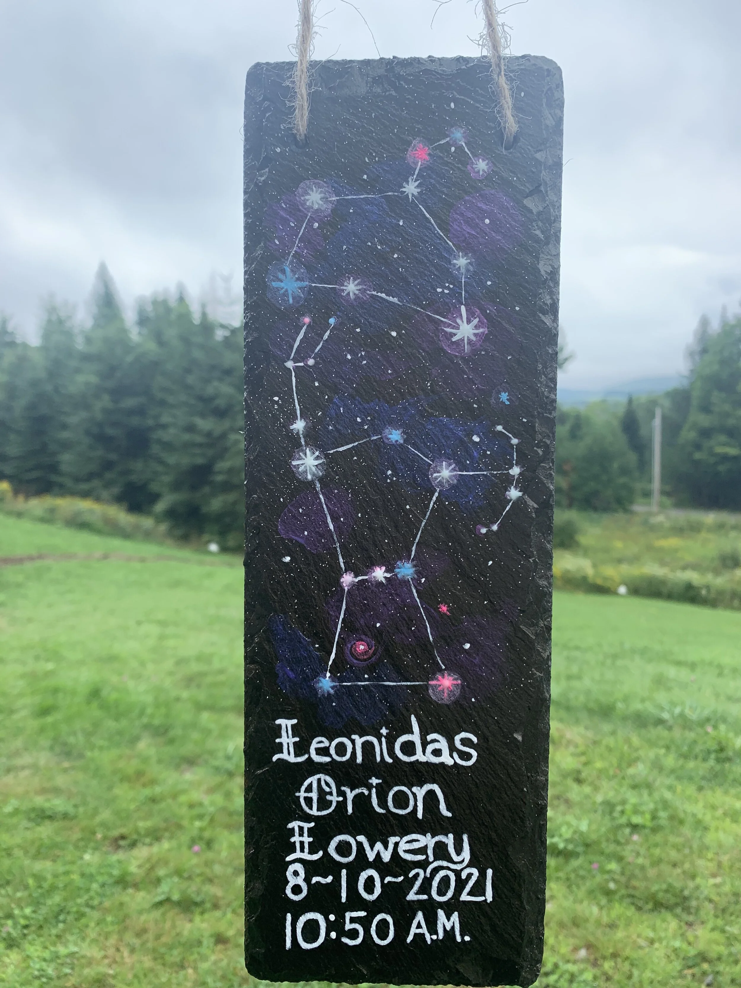 A painted black stone with a star constellation map, titled 'Leontidas Orion Flower'; it includes date '8-10-2021' and time '10:50 A.M.'