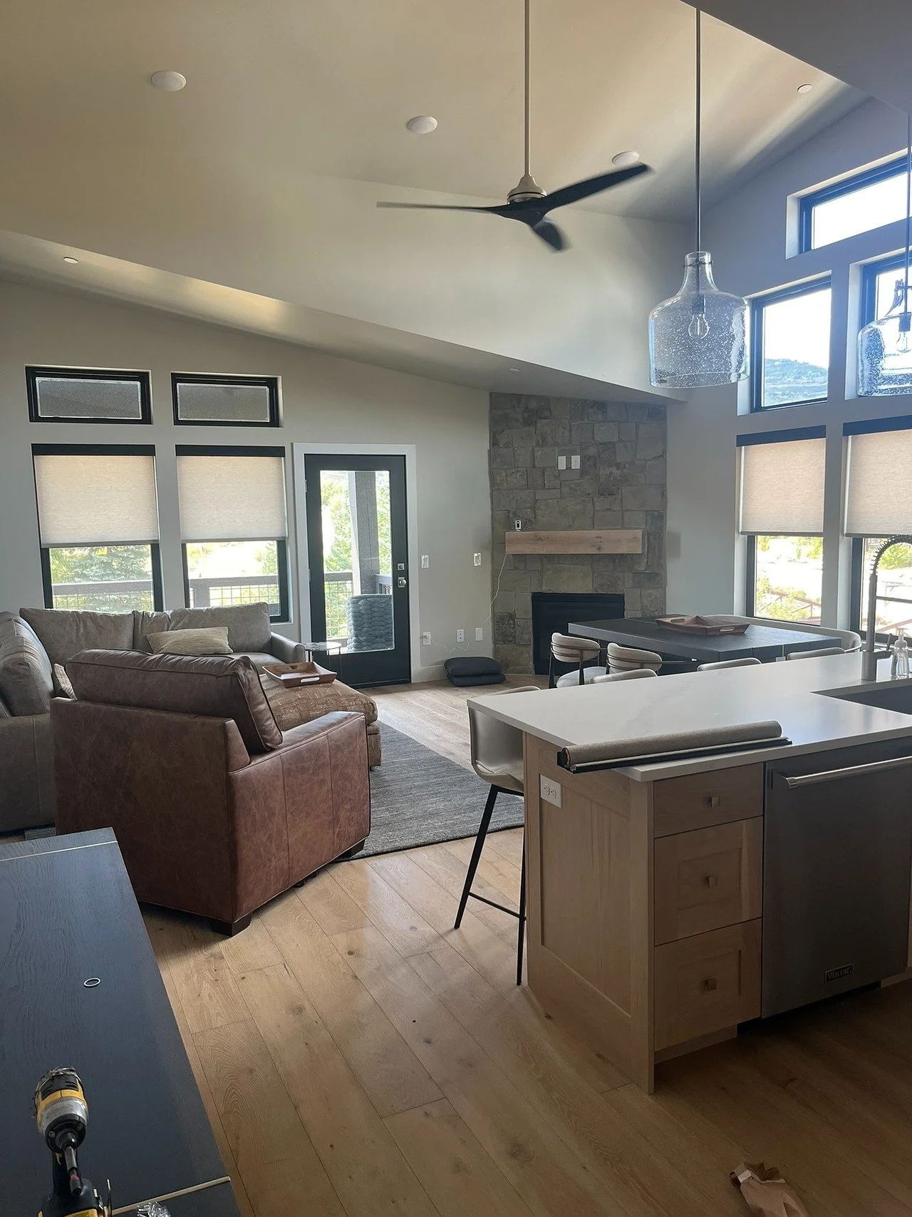 Living room with leather sofa, stone fireplace, large windows, and patio door leading outside, with kitchen island in foreground.