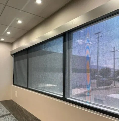 Interior view of a room with large window blinds covering wide windows, ceiling lights, and a neutral wall with a textured window sill.