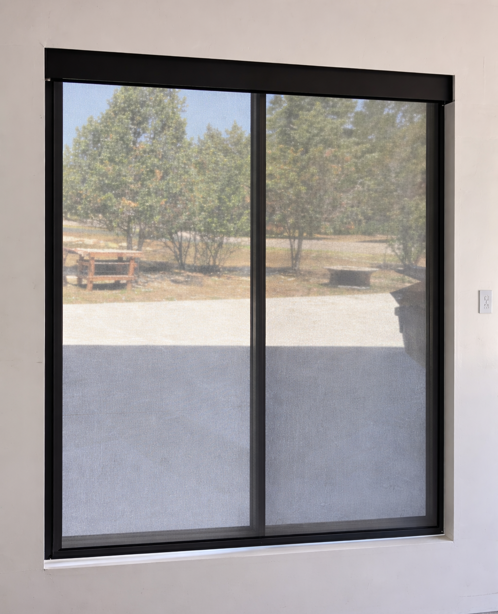 A sliding glass door with a screen view of a backyard garden with trees, a bench, and a fire pit.