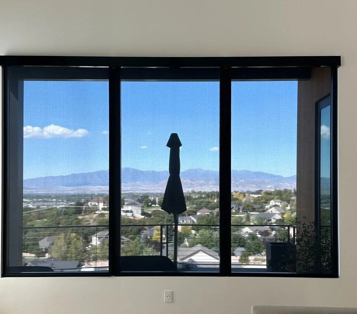 View from a large sliding glass door showing mountains in the distance, a partly cloudy sky, and rooftops of houses in a suburban neighborhood.