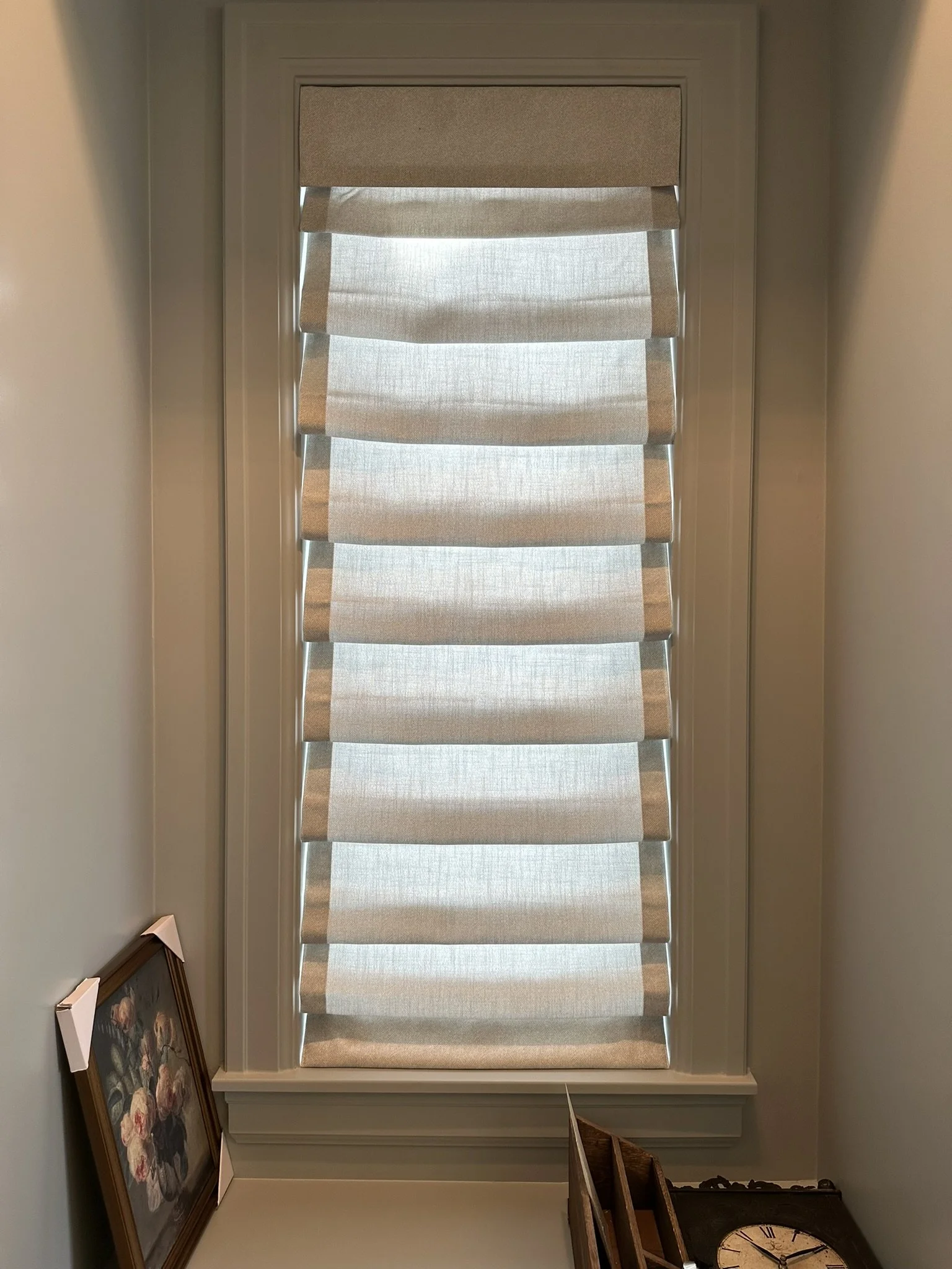 Close-up of a window with beige/rust-colored roman shades in a room.