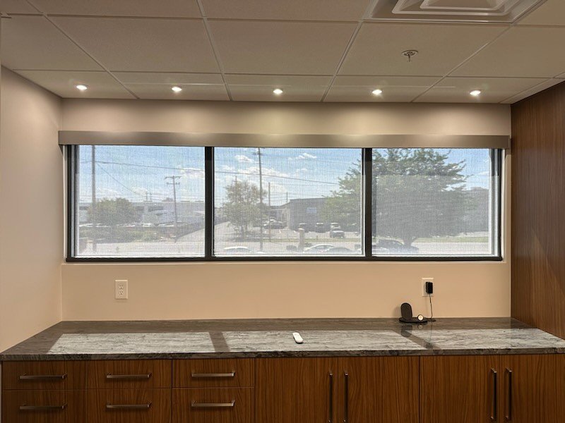 Empty room with a large window, granite countertop, and wooden cabinets.