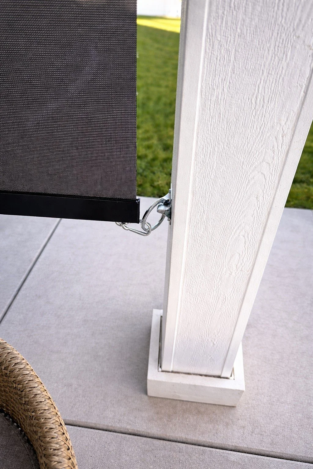 Close-up of a black outdoor privacy screen attached to a white wooden post on a patio, with grass visible in the background.