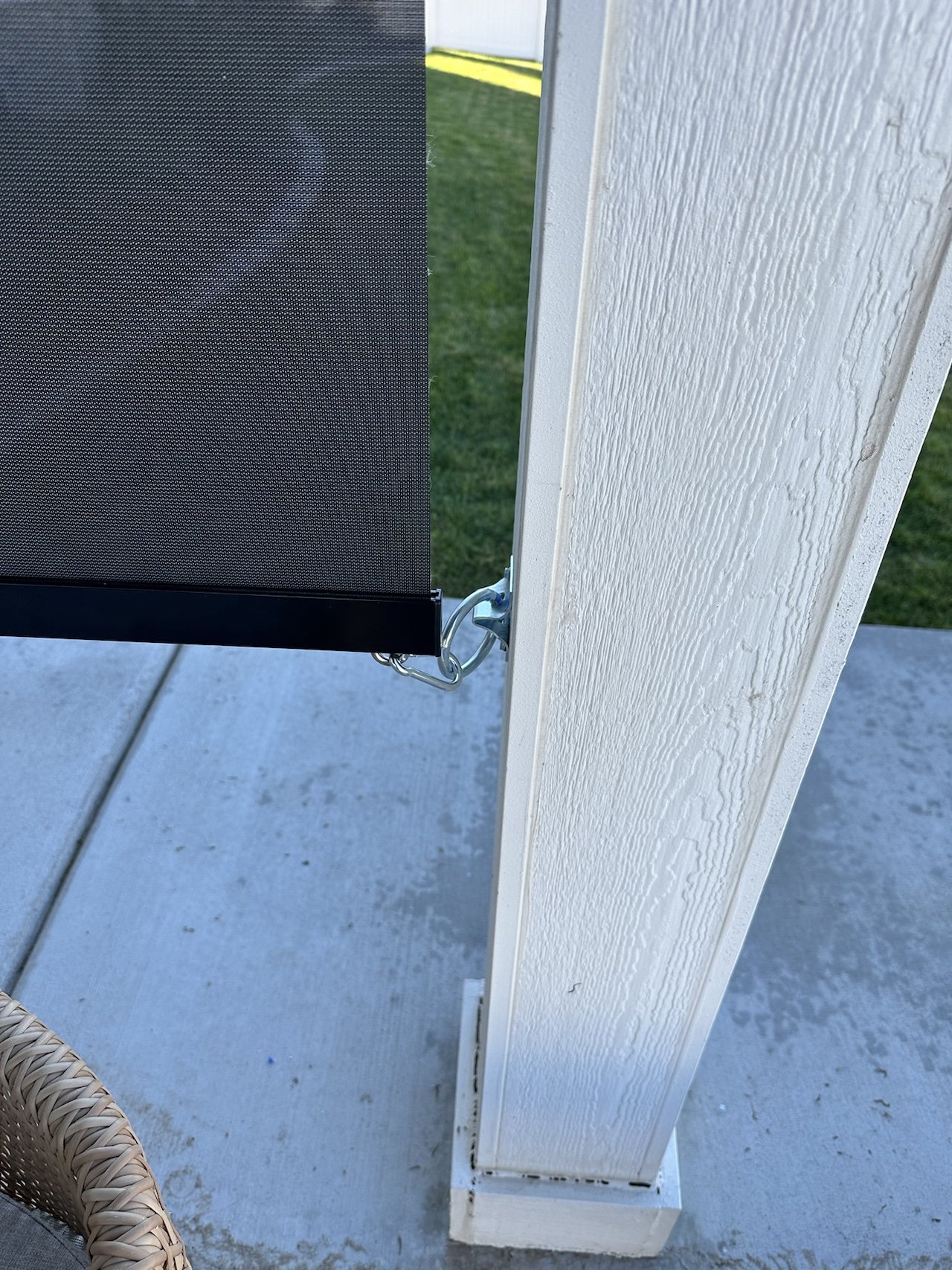 Close-up of an outdoor screened porch corner with a white wooden post, part of a black screen, and a metal hook secured to the post.