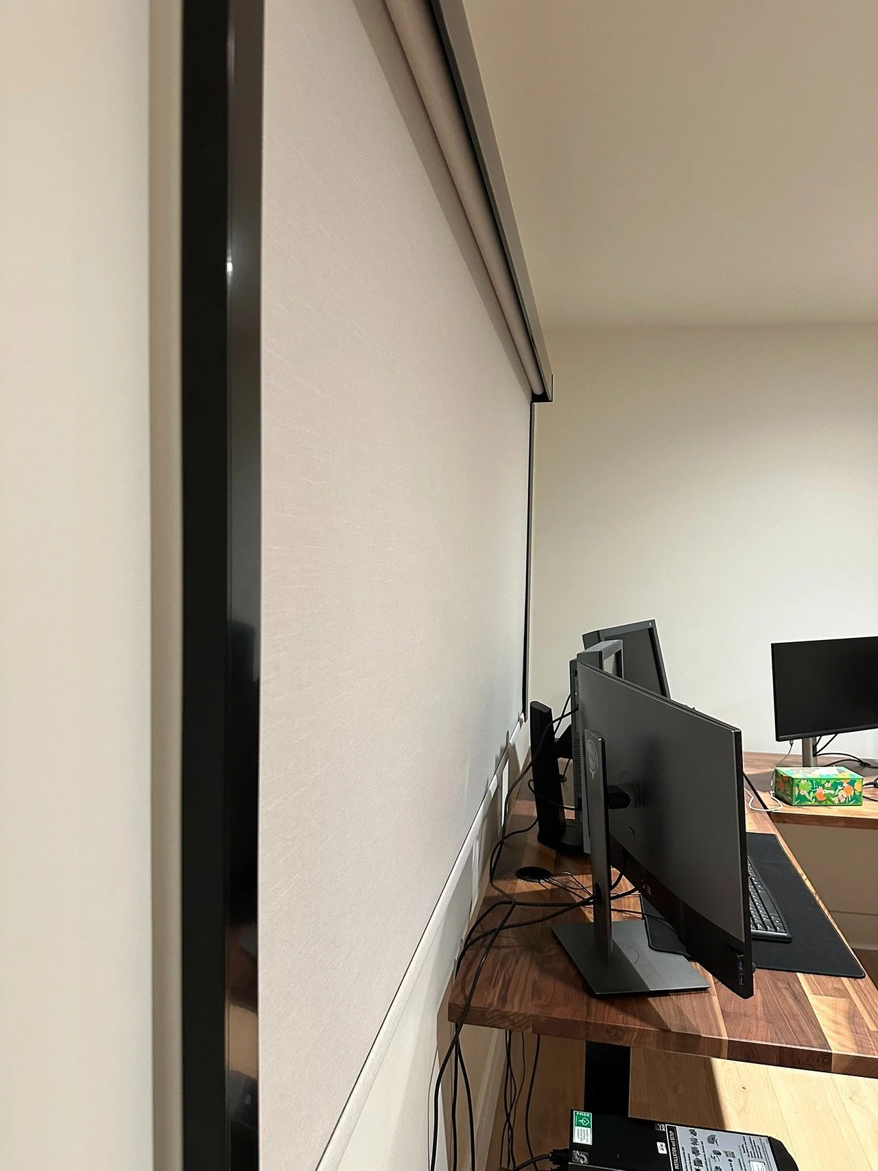 Office setup with a large white projection screen, two computer monitors, a keyboard, and a tissue box on the desk.
