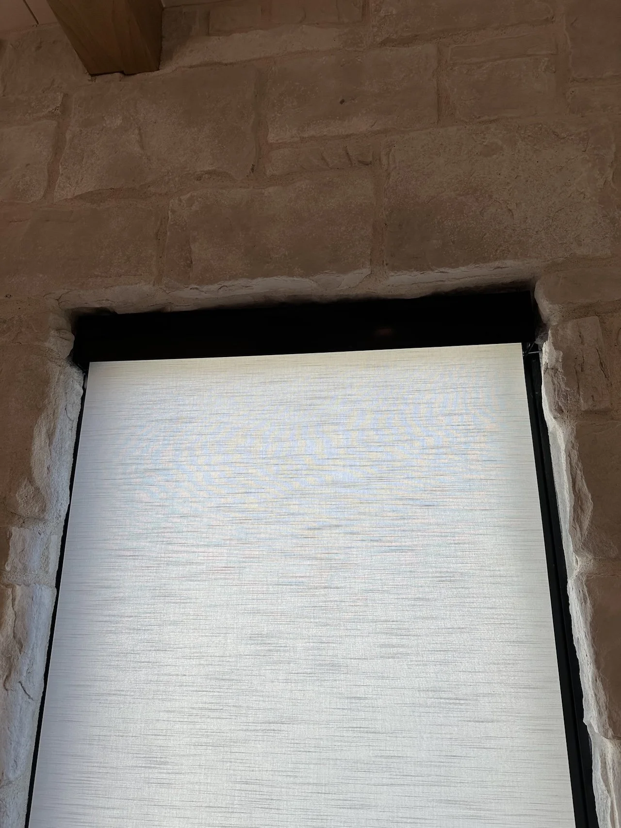 A window with a white textured shade set in a stone wall.