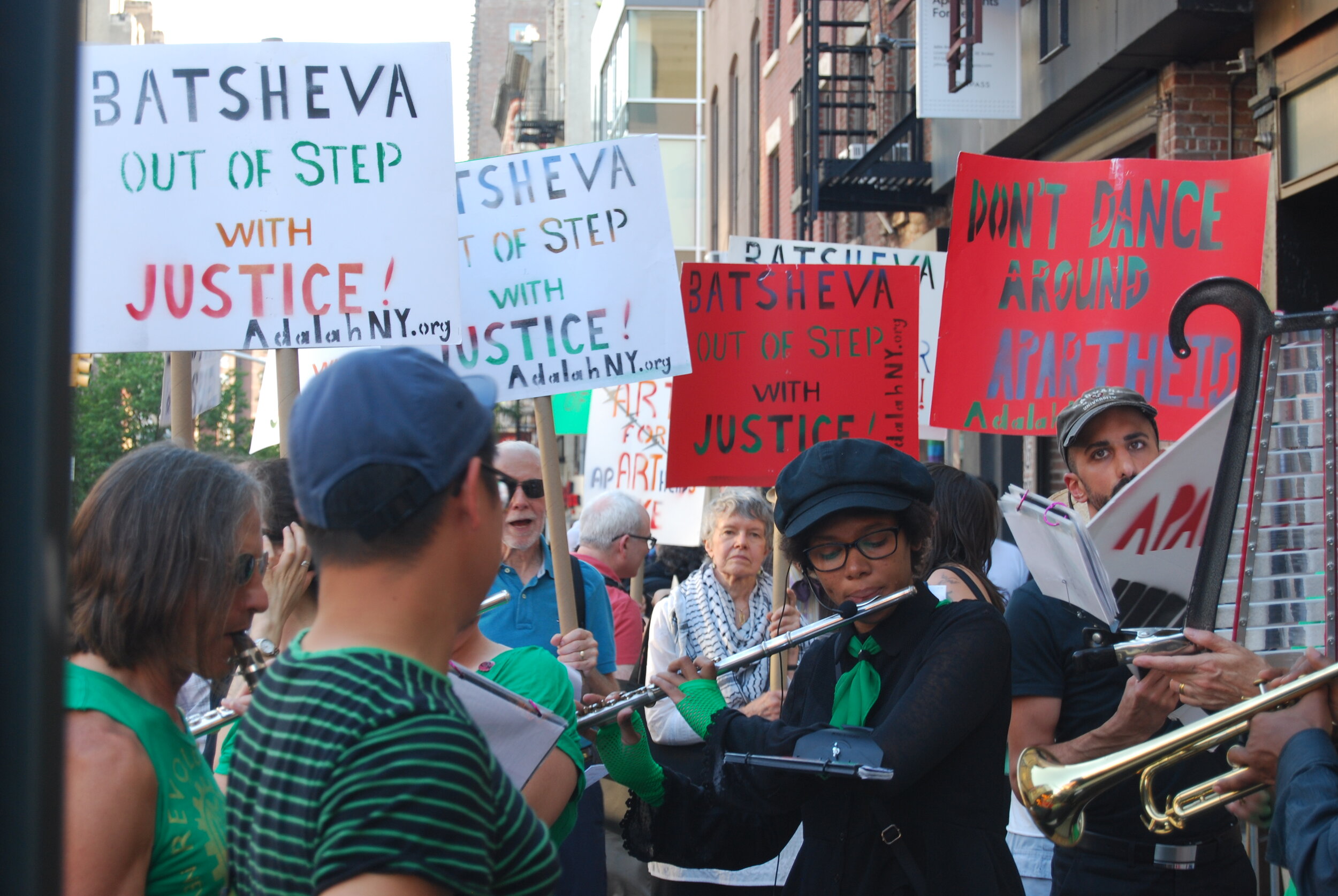  Protesters hold signs “Batsheva out of step with justice. One protester plays the flute. 