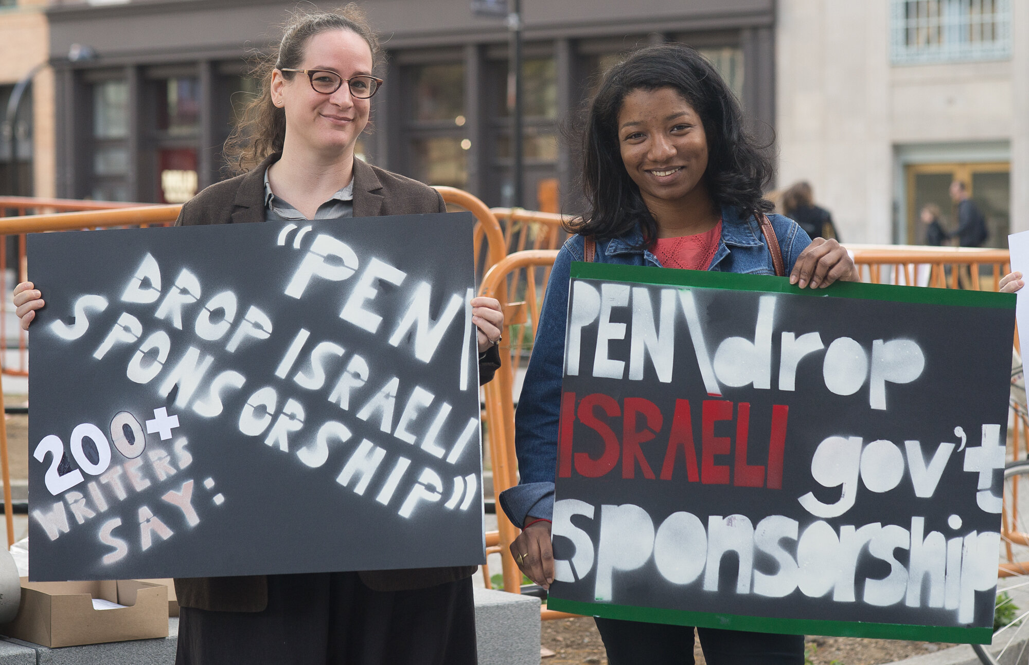  Two protesters smile and hold signs: “PEN: 200+ writers say, Drop Israeli government sponsorship” 
