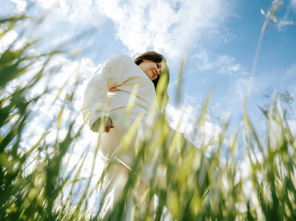 Woman walking in the field happy with a larger body and blue skies