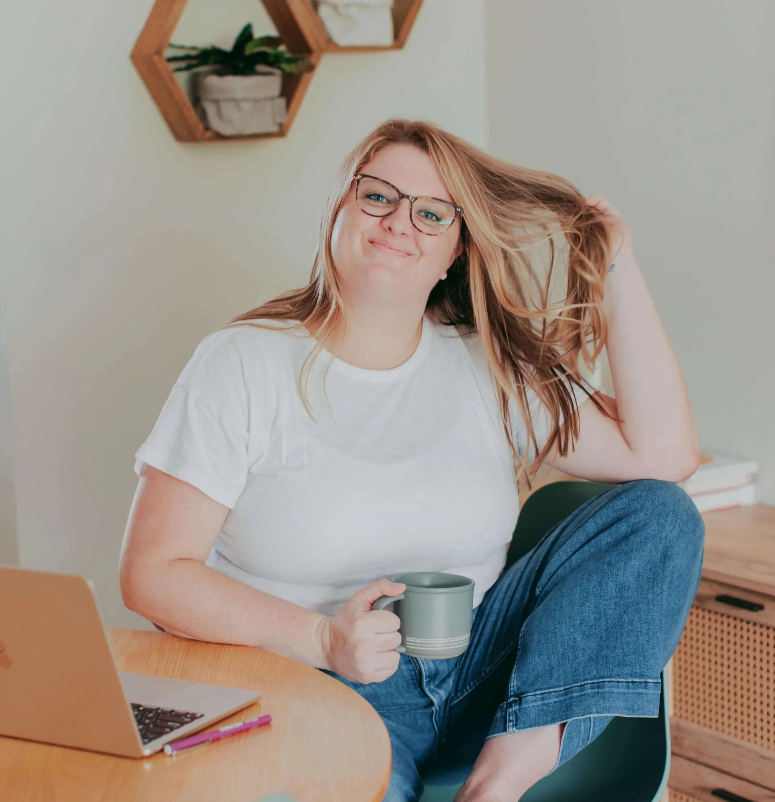 Image of woman with long blonde hair drinking coffee at their therapist desk smiling in glasses