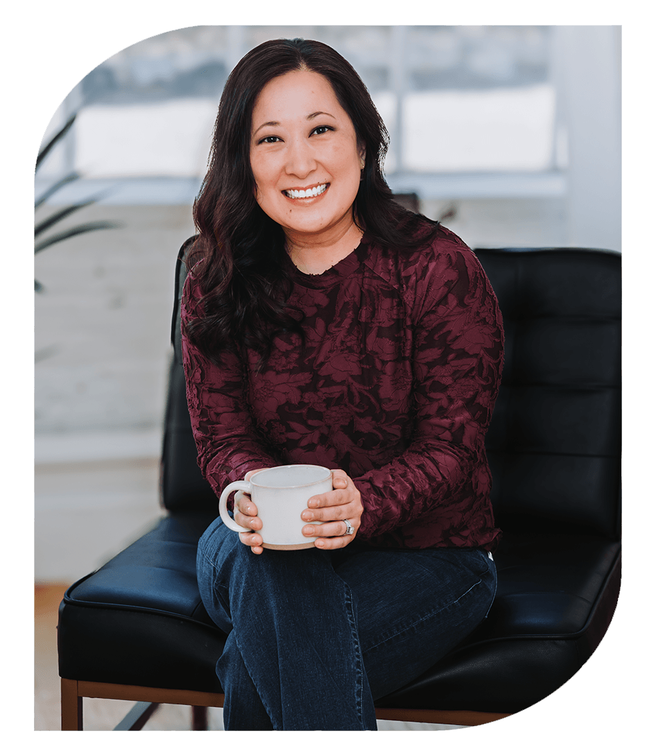 Lisa Perlock, MA, LPCC, CCTP, sitting on a chair holding a mug