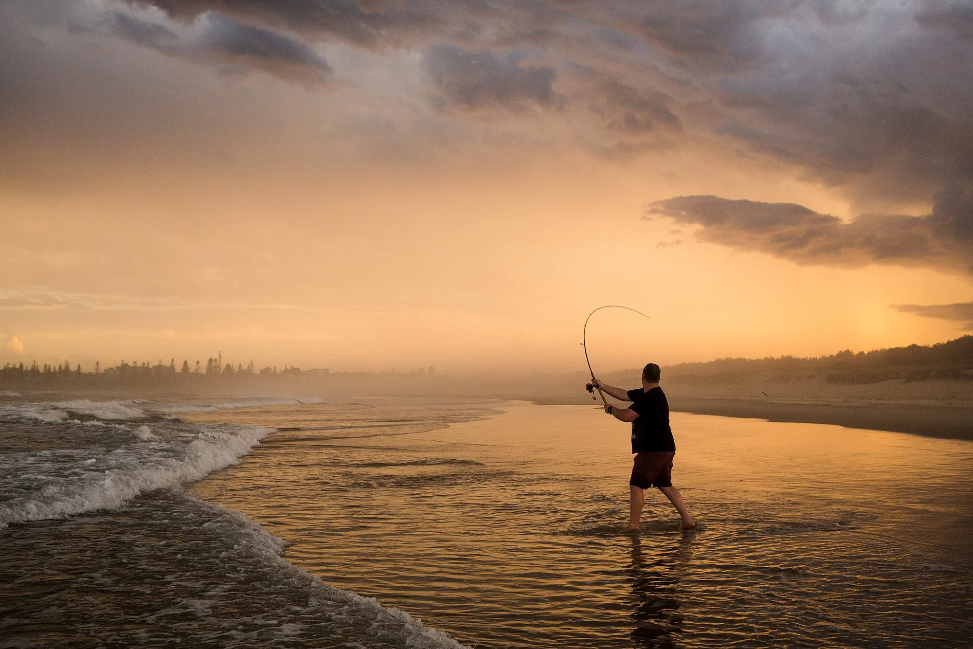 A man fishing in the ocean during sunset.