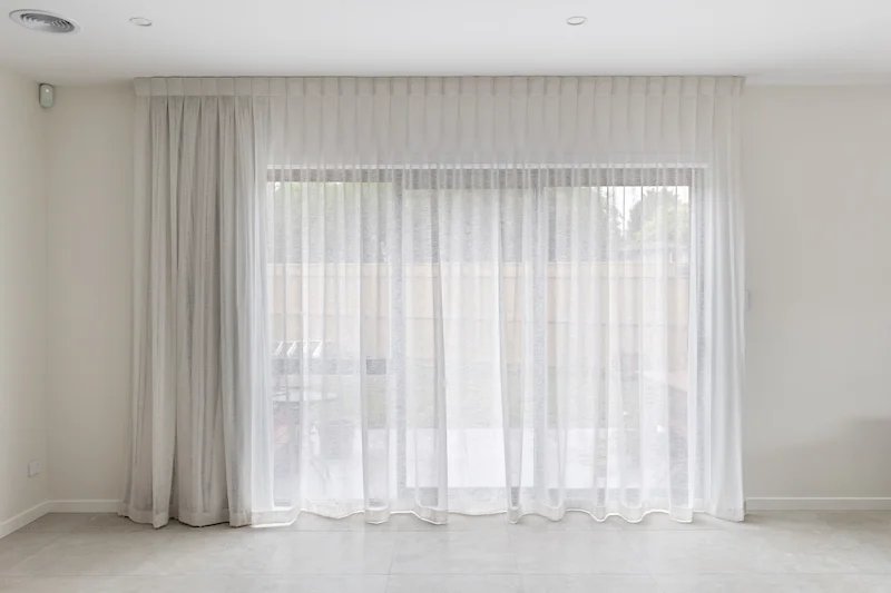 White curtains hanging in front of glass sliding door leading to outdoor patio