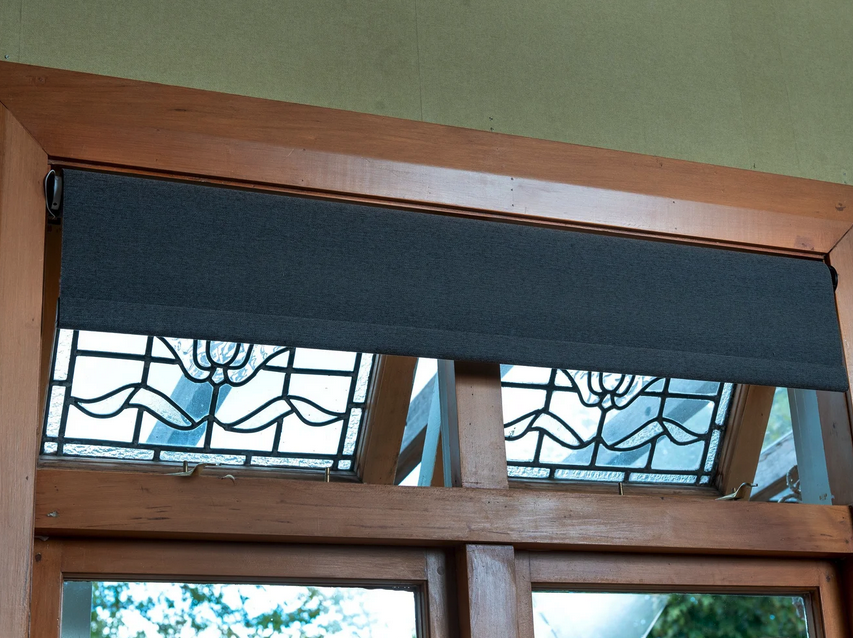 Decorative stained glass windows with floral design above a wooden door or window frame, partially covered by a charcoal gray roller blind.