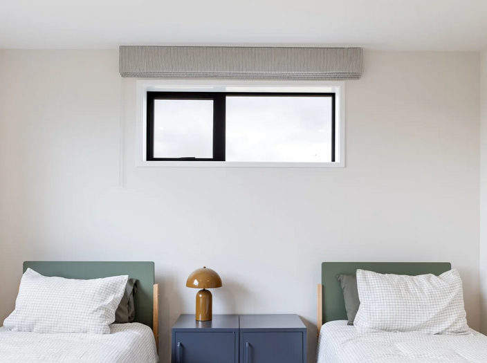 Bedroom with 2 beds and a side tables between with a roman blind pulled up on the window