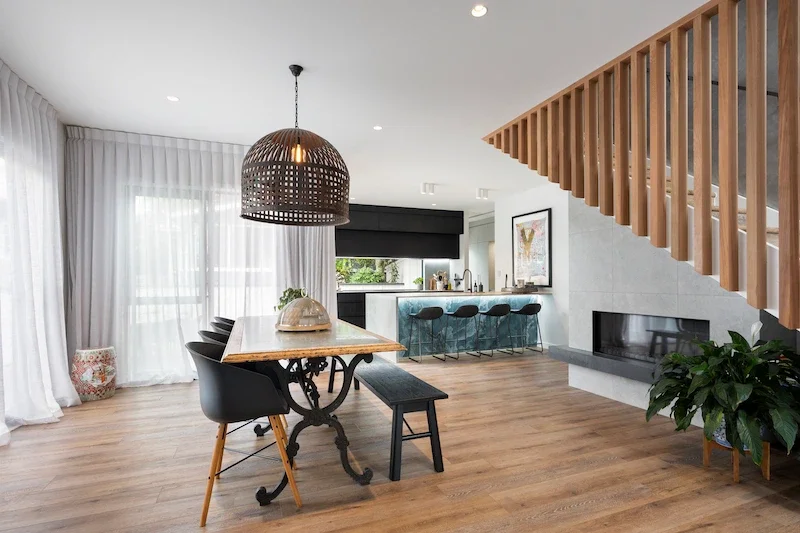 Modern open-concept living space with wood flooring, a dining area, a kitchen with a breakfast bar, and a staircase with wooden railing.