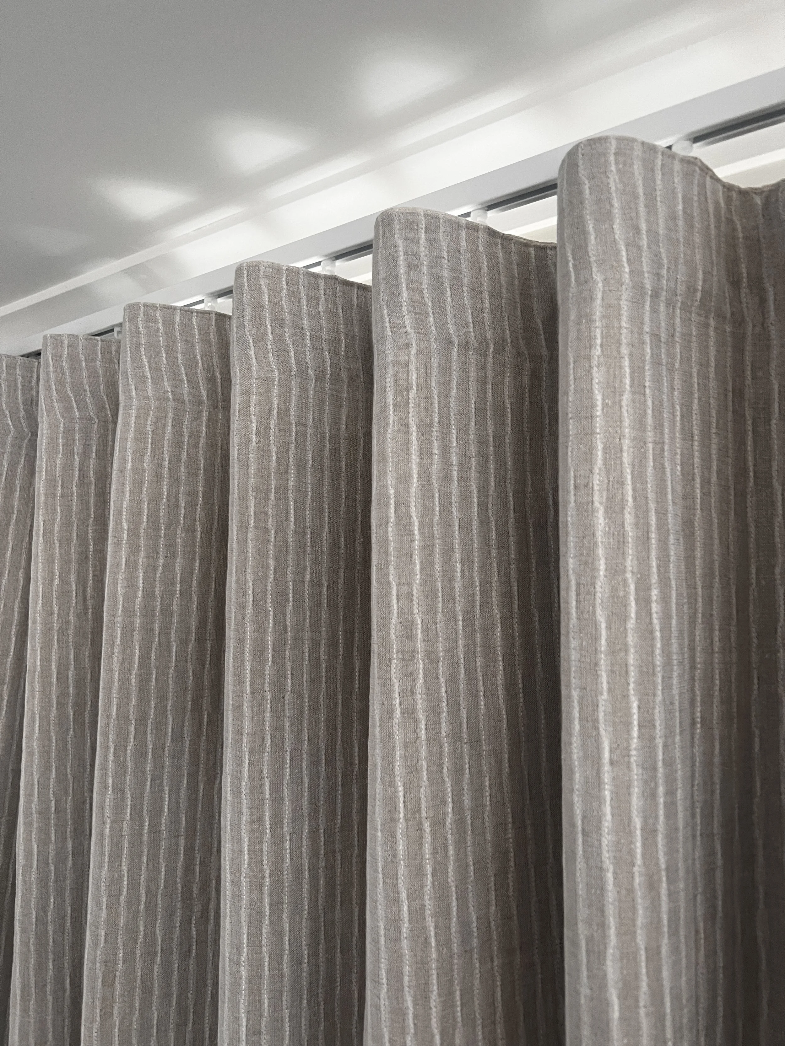 Close-up of beige curtains with vertical white stripes hanging in front of a window.