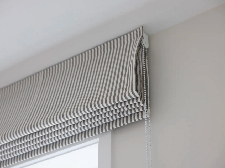 A window with a striped fabric Roman shade and a beaded chain pull.