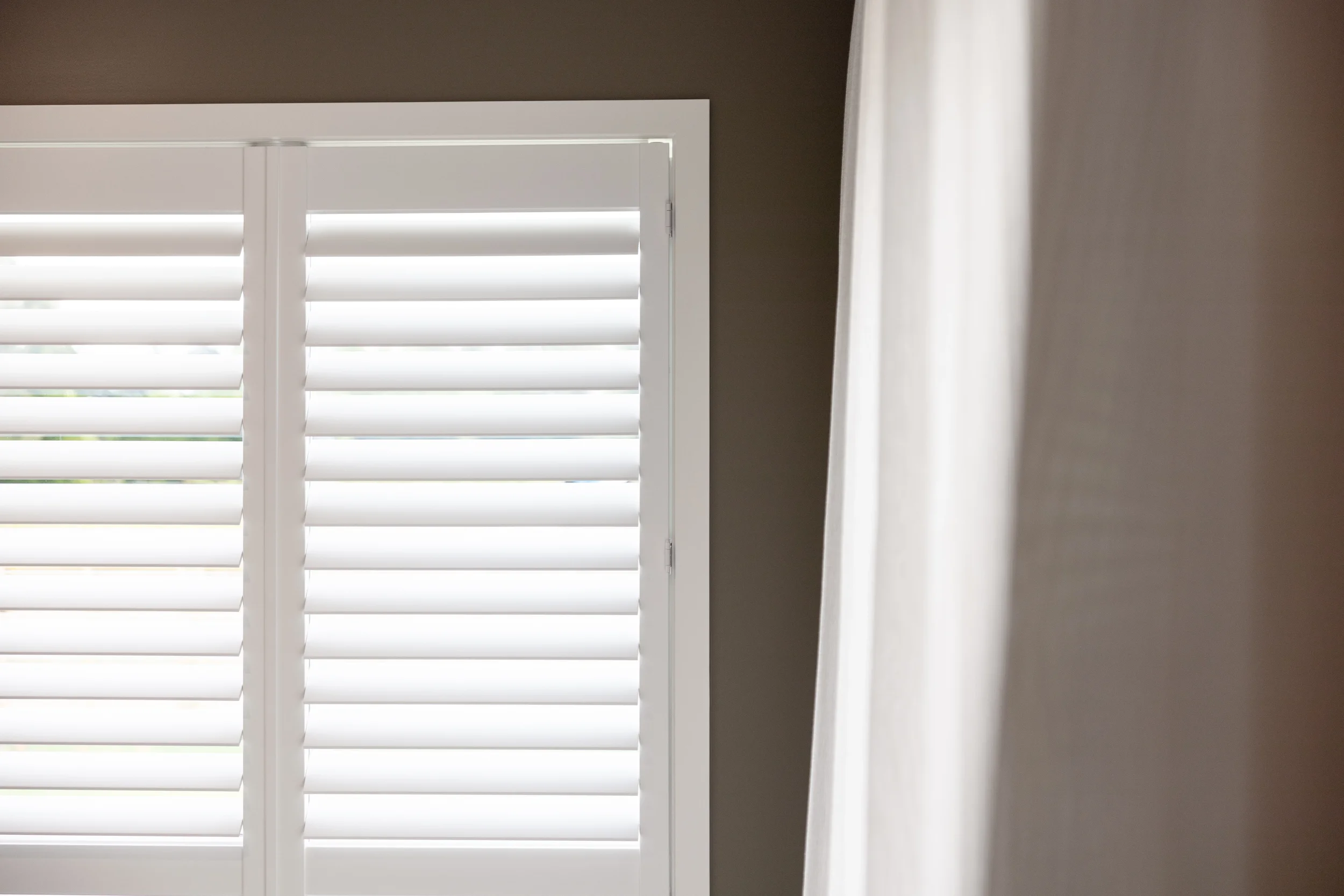 Close-up of a window with white plantation shutters and a white curtain on the right side