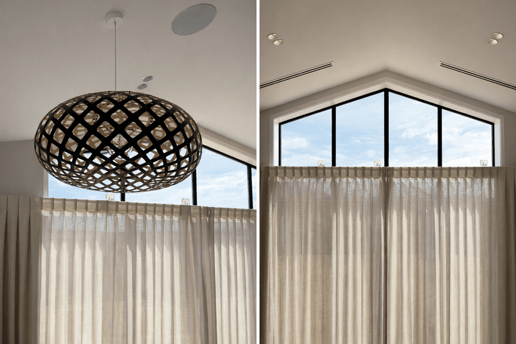 Interior view of a room with high ceilings, a large window with a triangular top, beige curtains, and a decorative pendant light.