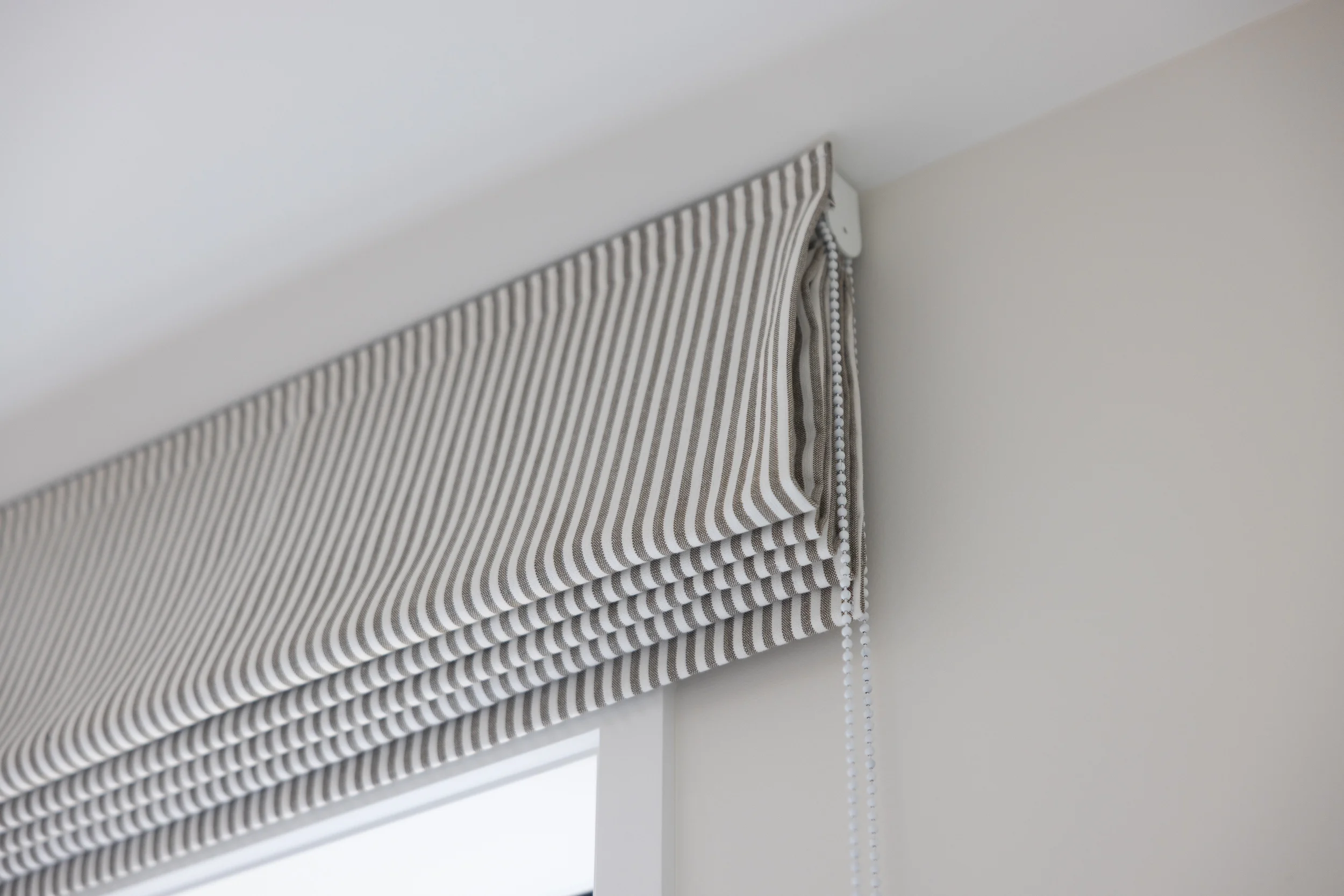 A window with a striped fabric Roman shade and a beaded chain pull.