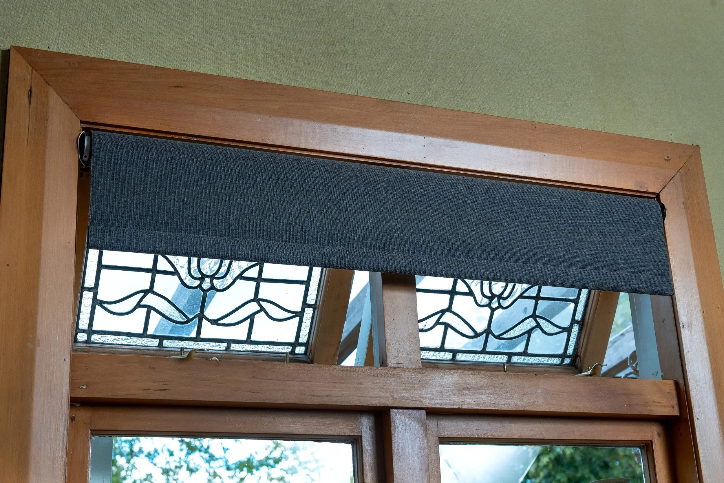 Decorative stained glass windows with floral design above a wooden door or window frame, partially covered by a charcoal gray roller blind.
