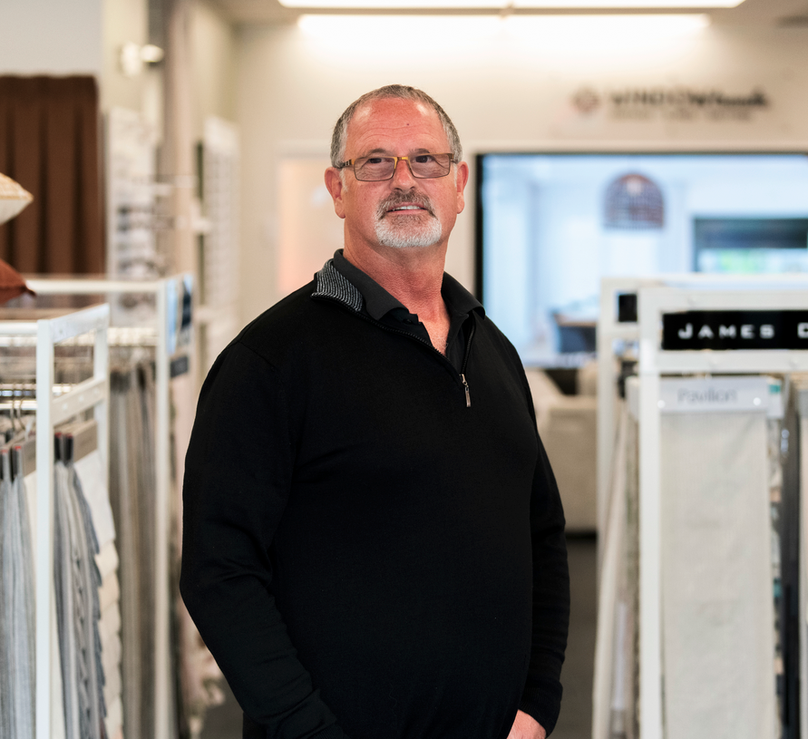 Interior view of large windows with partly closed blinds, showing an outdoor scene with trees, blue sky, and construction dirt.