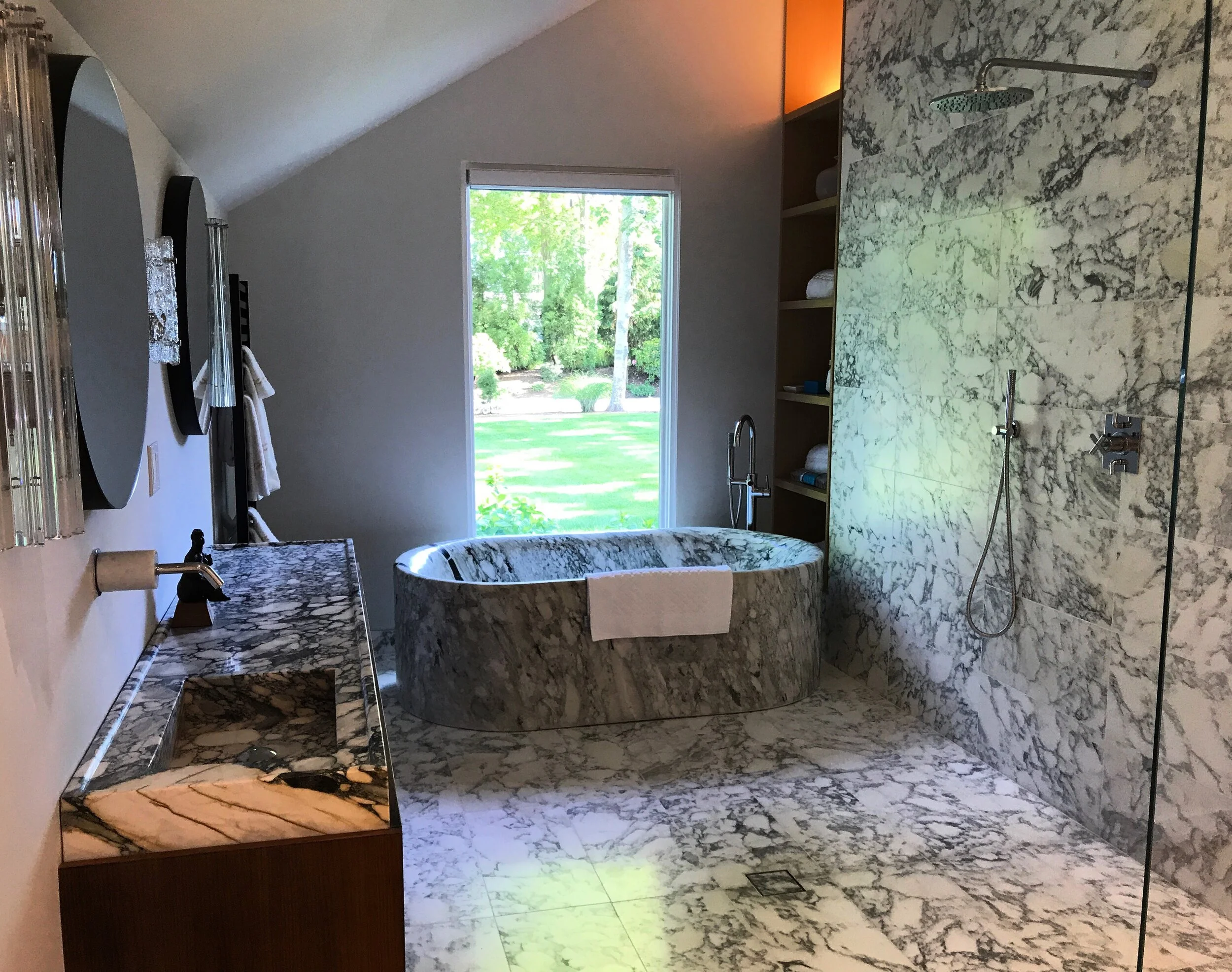 A luxurious bathroom designed in Southampton NY with marble tiles and a freestanding marble bathtub. 