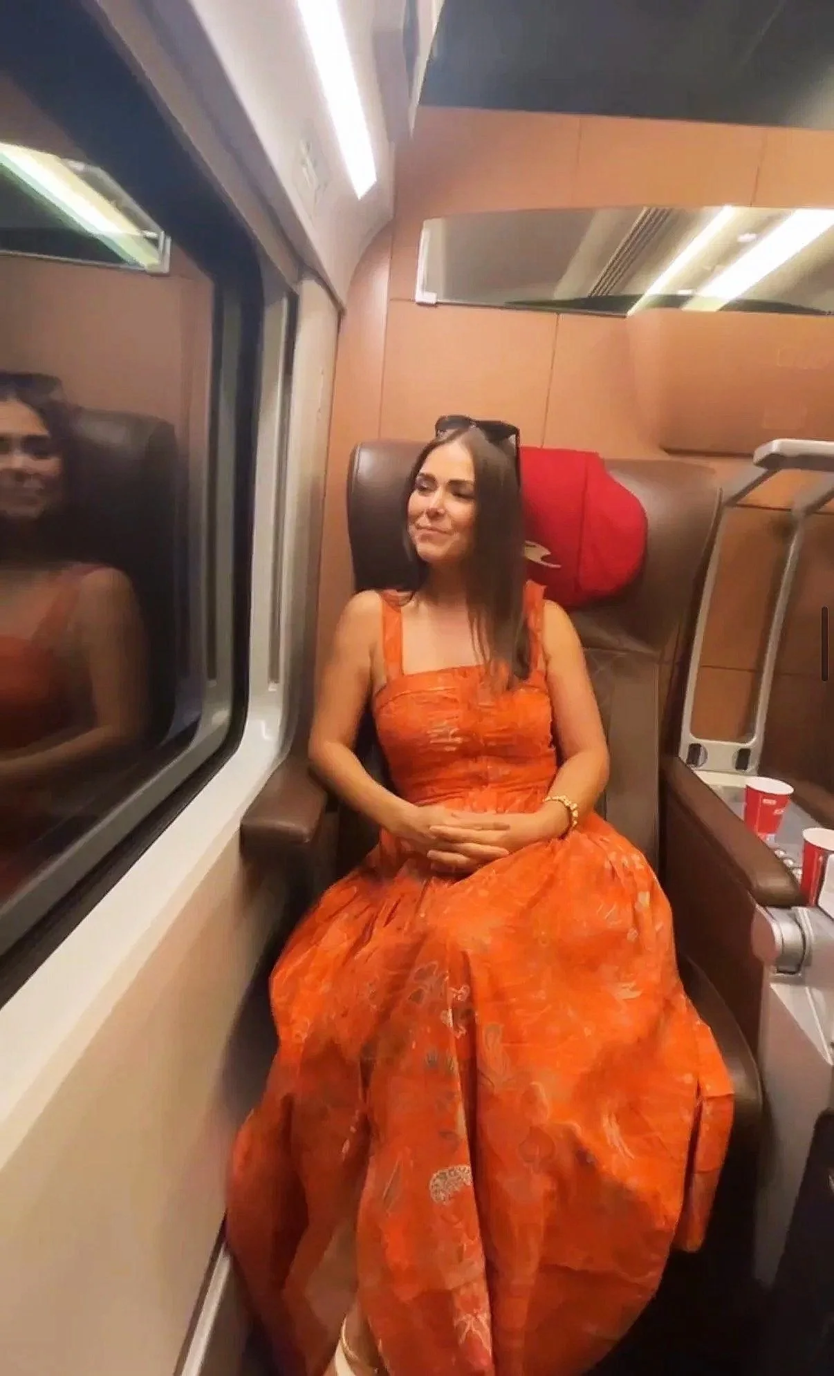 Quinn Hannum in an orange dress sitting on a train traveling from Florance to Rome, Italy.