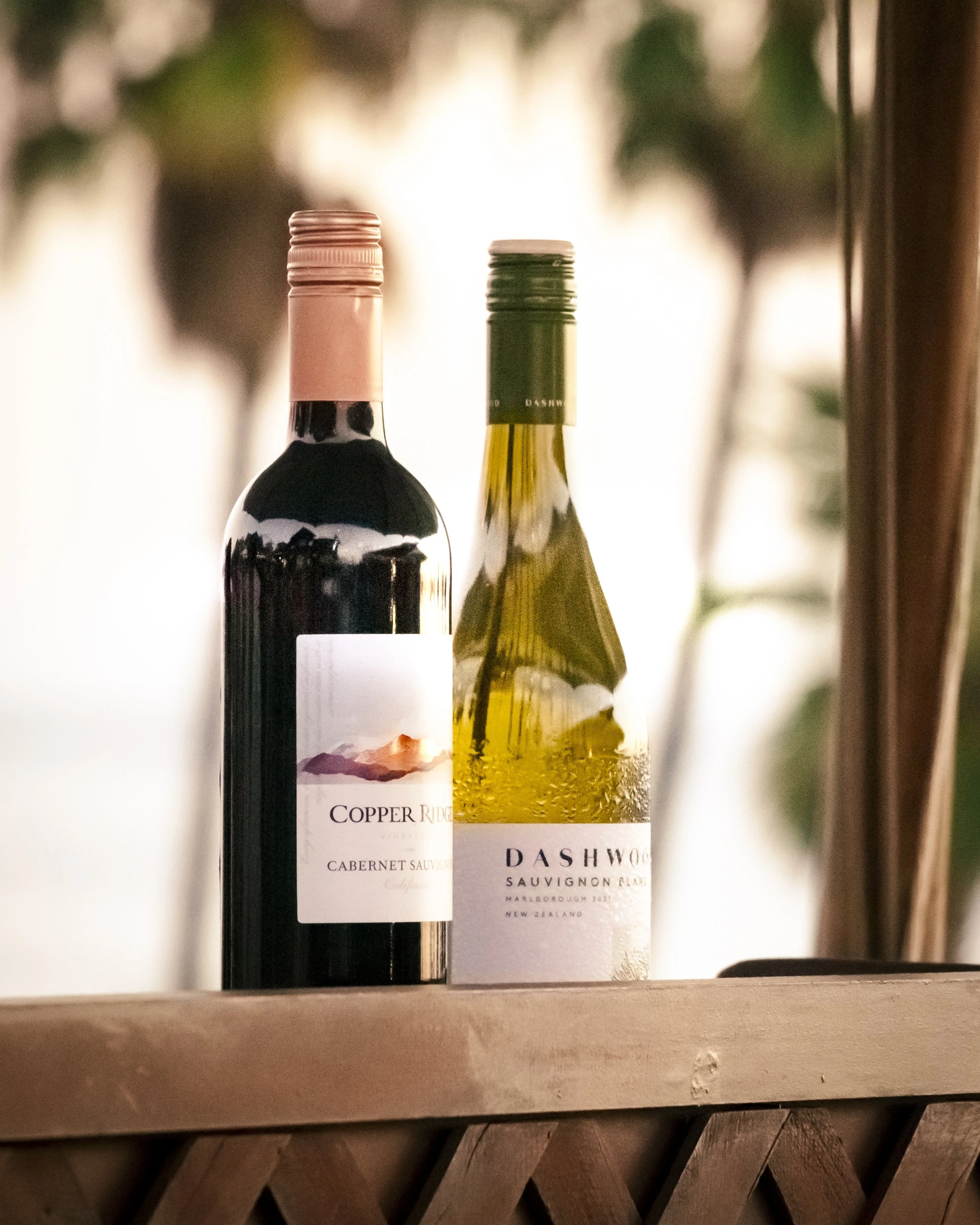 Two bottles of wine on a wooden surface, one is a red Cabernet Sauvignon and the other is a white Sauvignon Blanc.