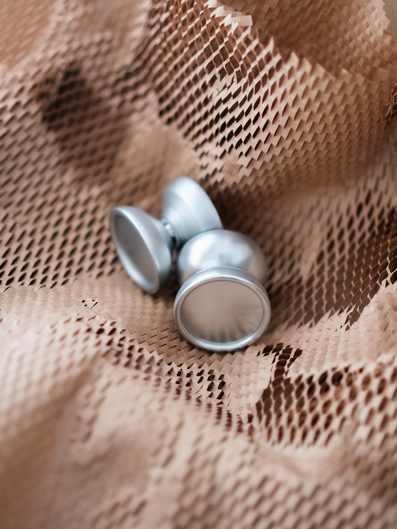 Two silver yo-yos nested in honeycomb kraft packing paper