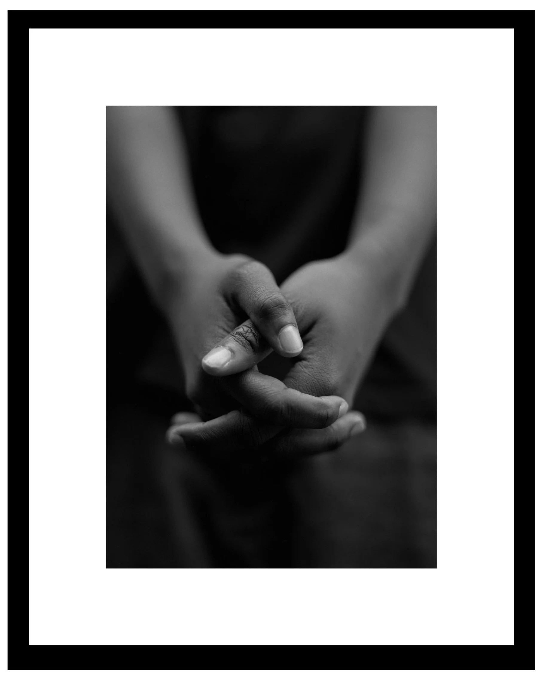 Black and white photo of person's hands clasped together on a reflective surface.