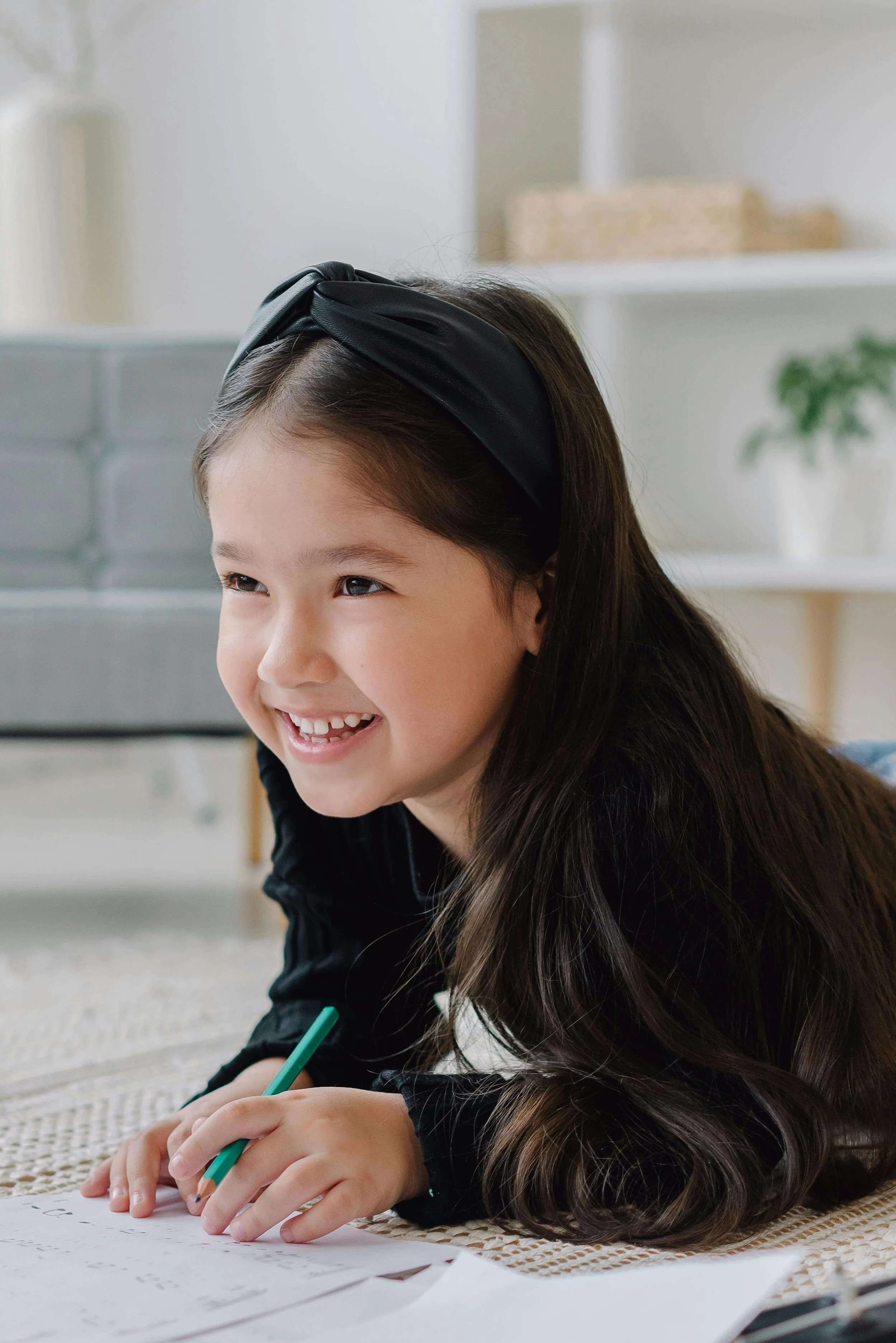 Young child smiling while lying on the floor and drawing with a pencil on paper. Child therapy encourages emotional expression, creativity, and confidence through age-appropriate activities that help children thrive.