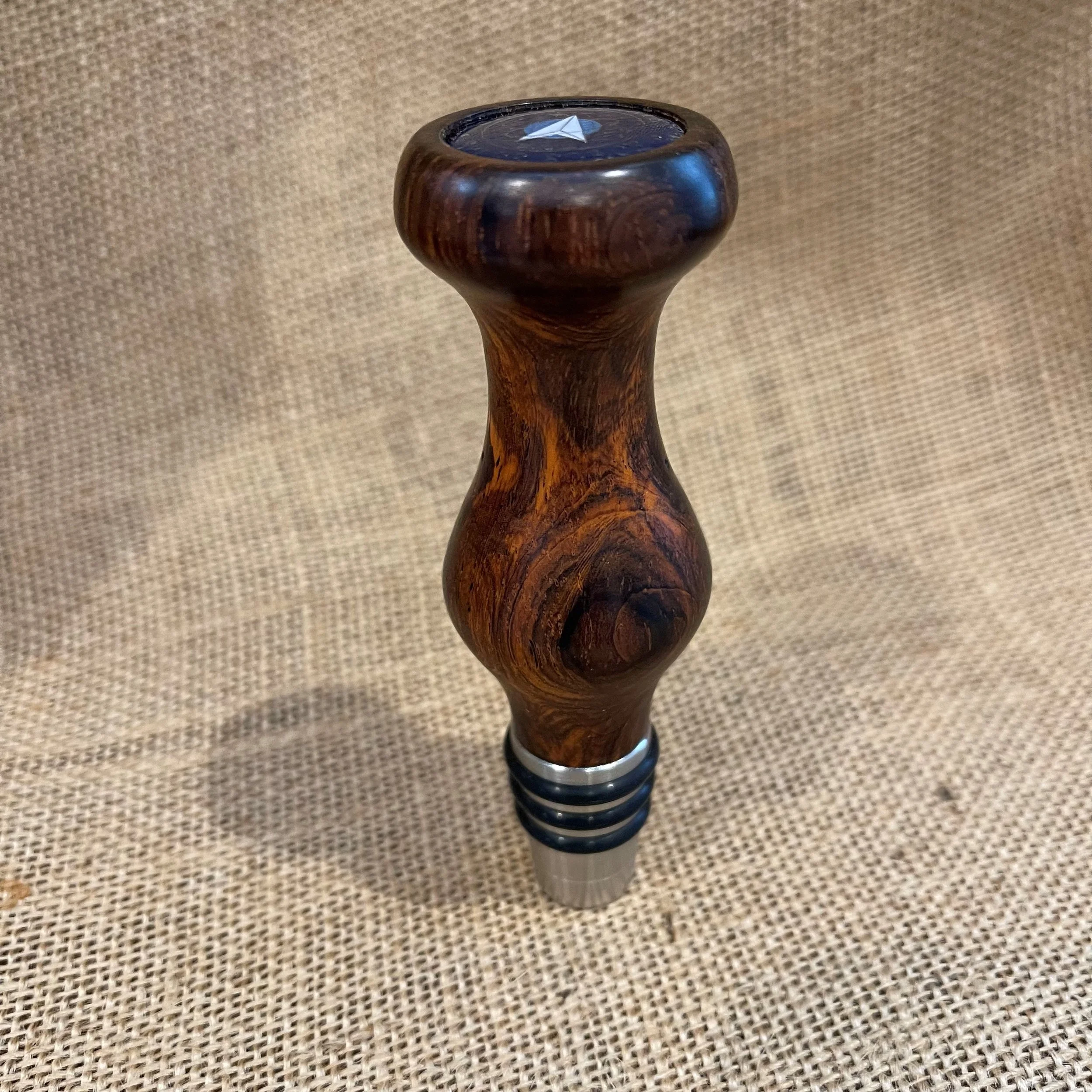 Handcrafted cocobolo whiskey bottle topper with rich red-brown grain and polished curves, set against a burlap background.