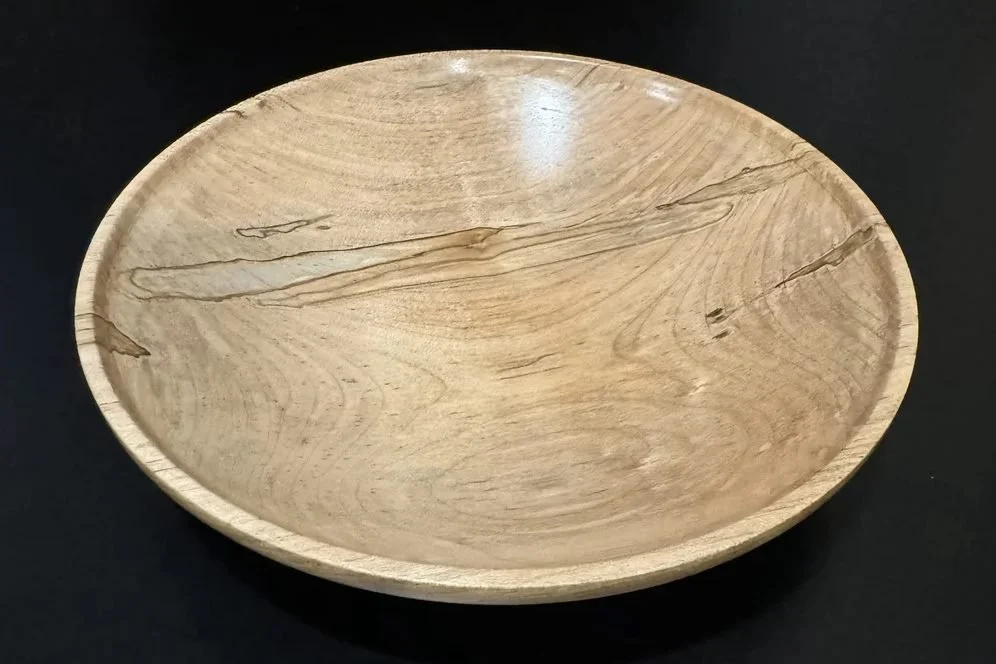 A shallow dish turned from spalted pecan, showing light tones with subtle spalting lines across the grain.