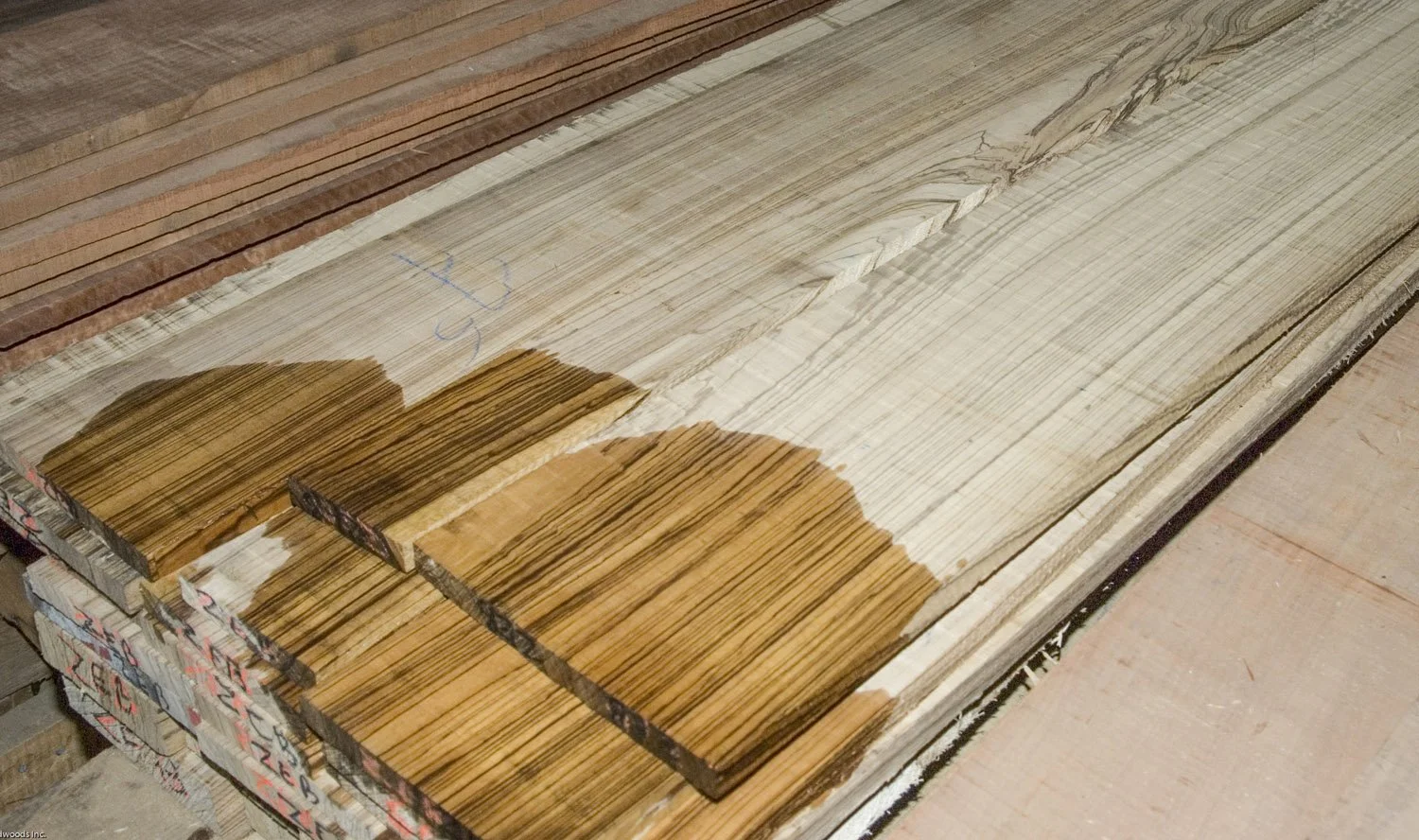 Stack of Zebrawood boards showing their natural striped grain, with sections wetted to reveal the bold contrast of light and dark lines.