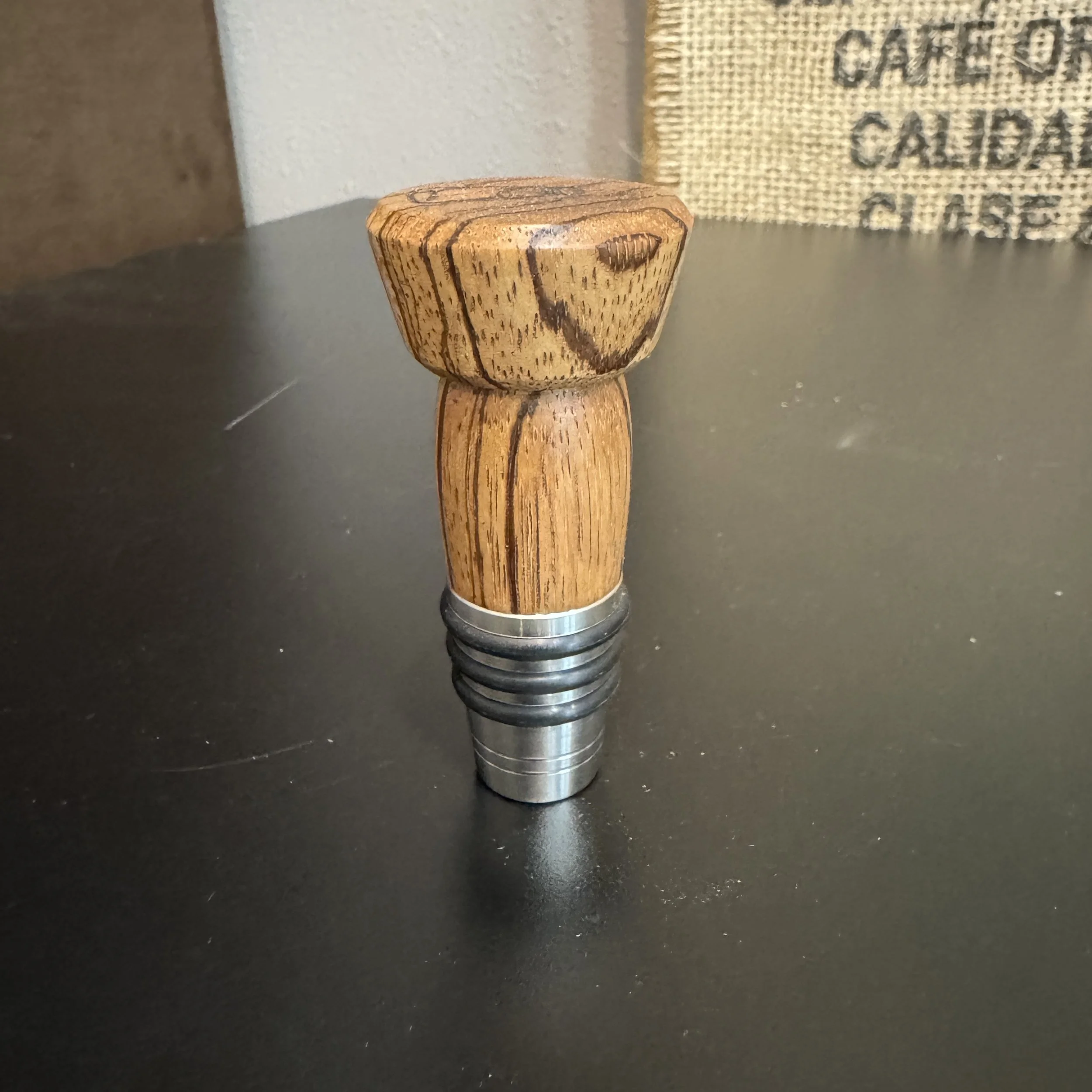 A handcrafted Zebrawood whiskey topper with bold striped grain and a stainless steel base.