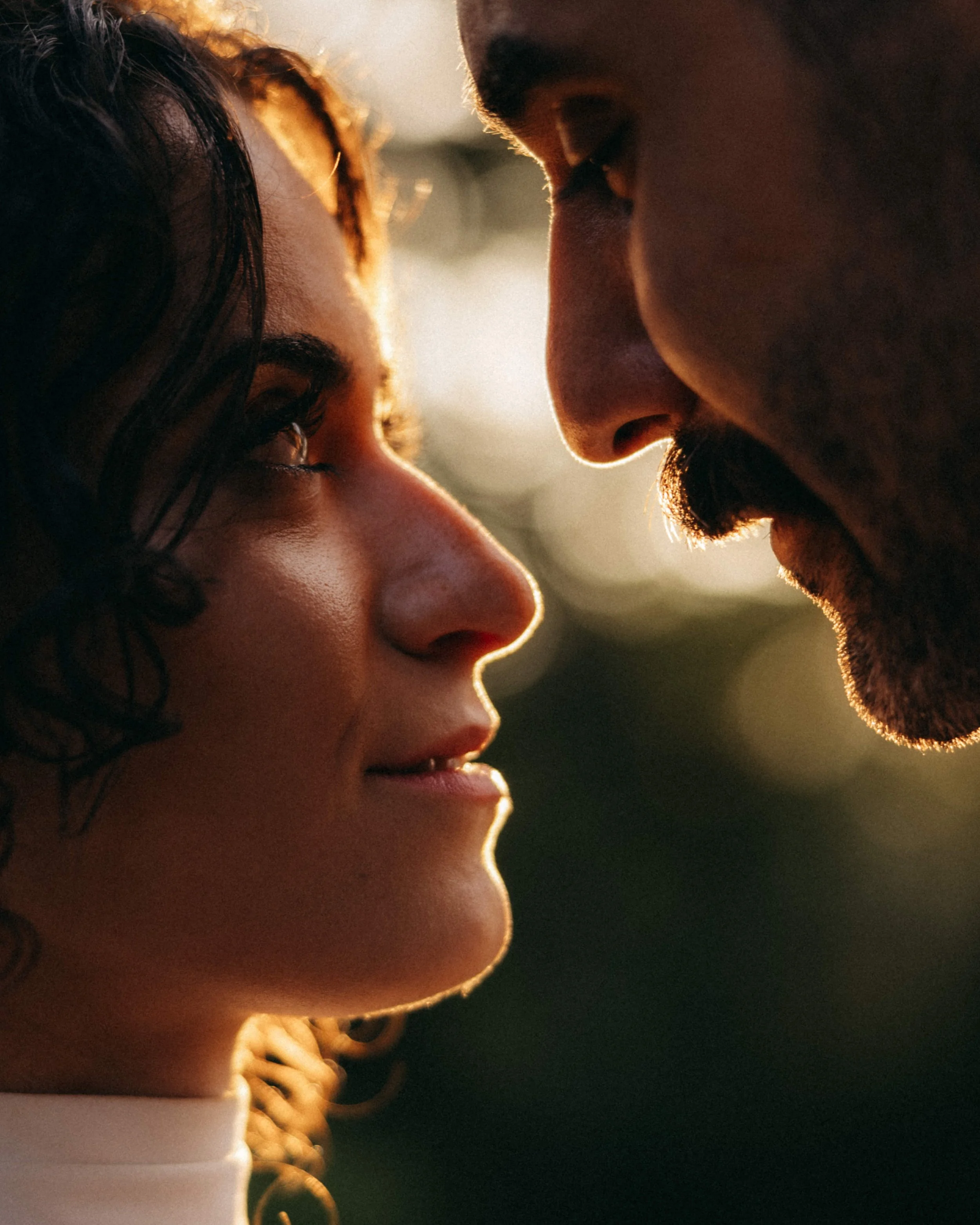 A close-up of a man and woman face-to-face with foreheads touching, in warm sunlight.