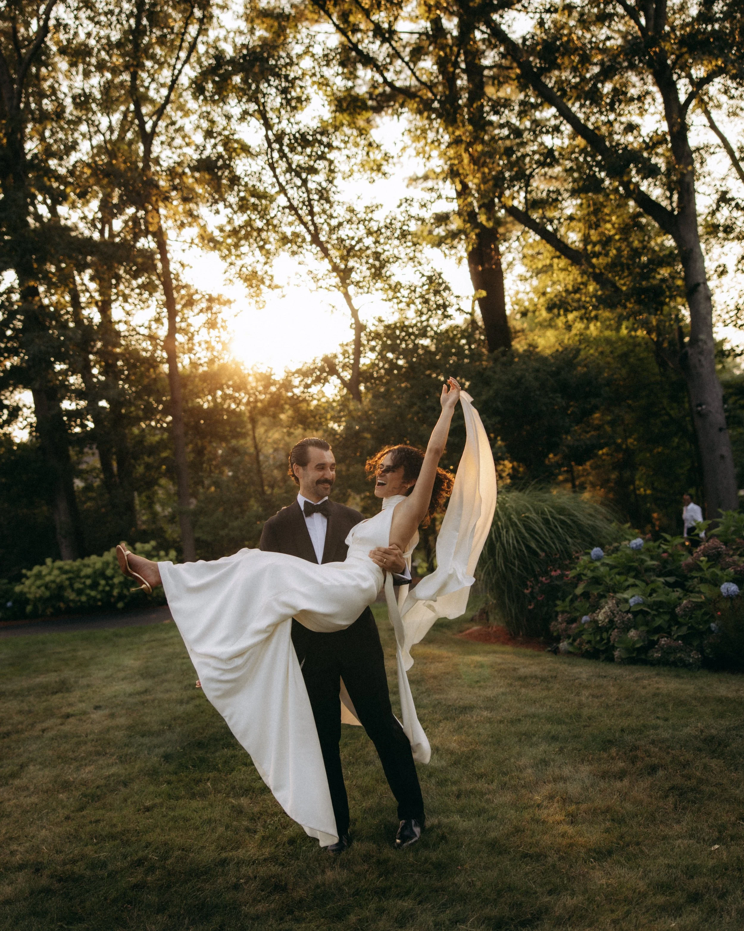 A man and woman in formal attire dancing outdoors at sunset.