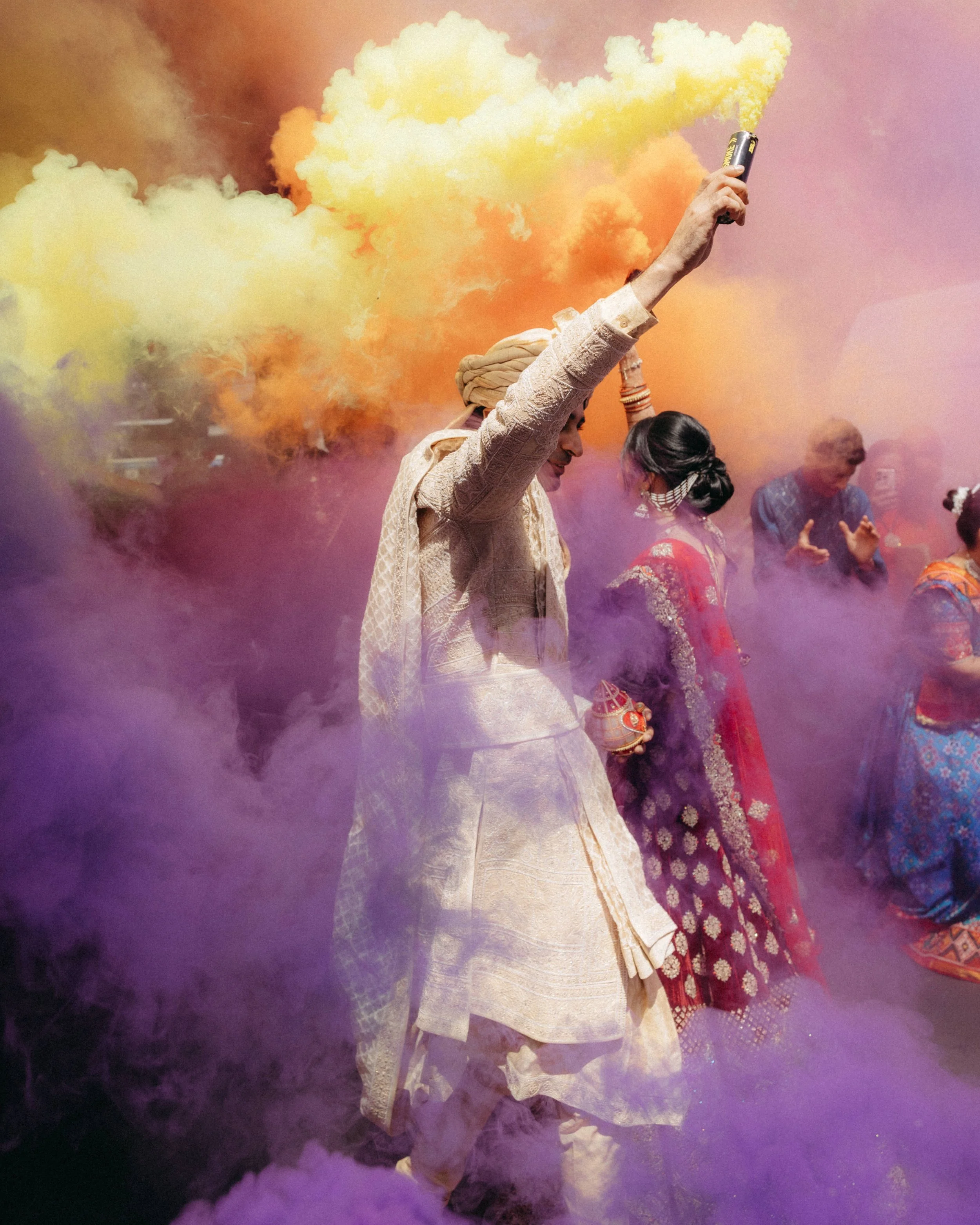 People celebrating with colored powder and smoke, dressed in traditional Indian attire, during a festival.