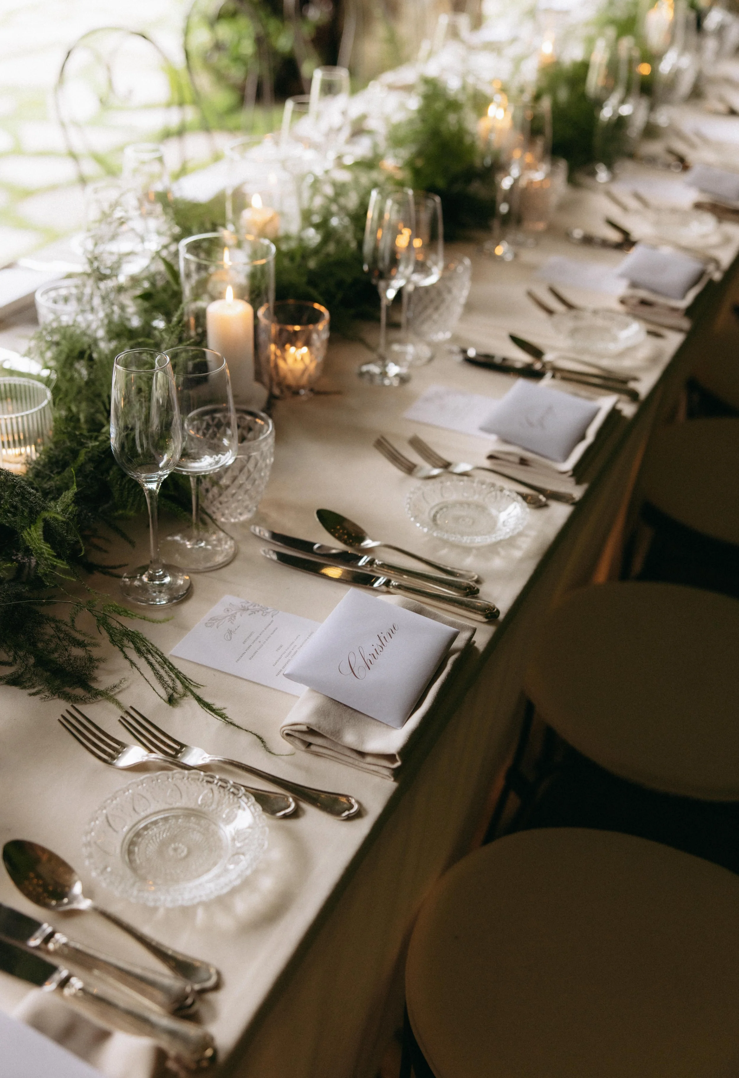 A close-up of a decorated banquet table with candles, glassware, cutlery, and place cards, including a visible place card with the name 'Christina'.