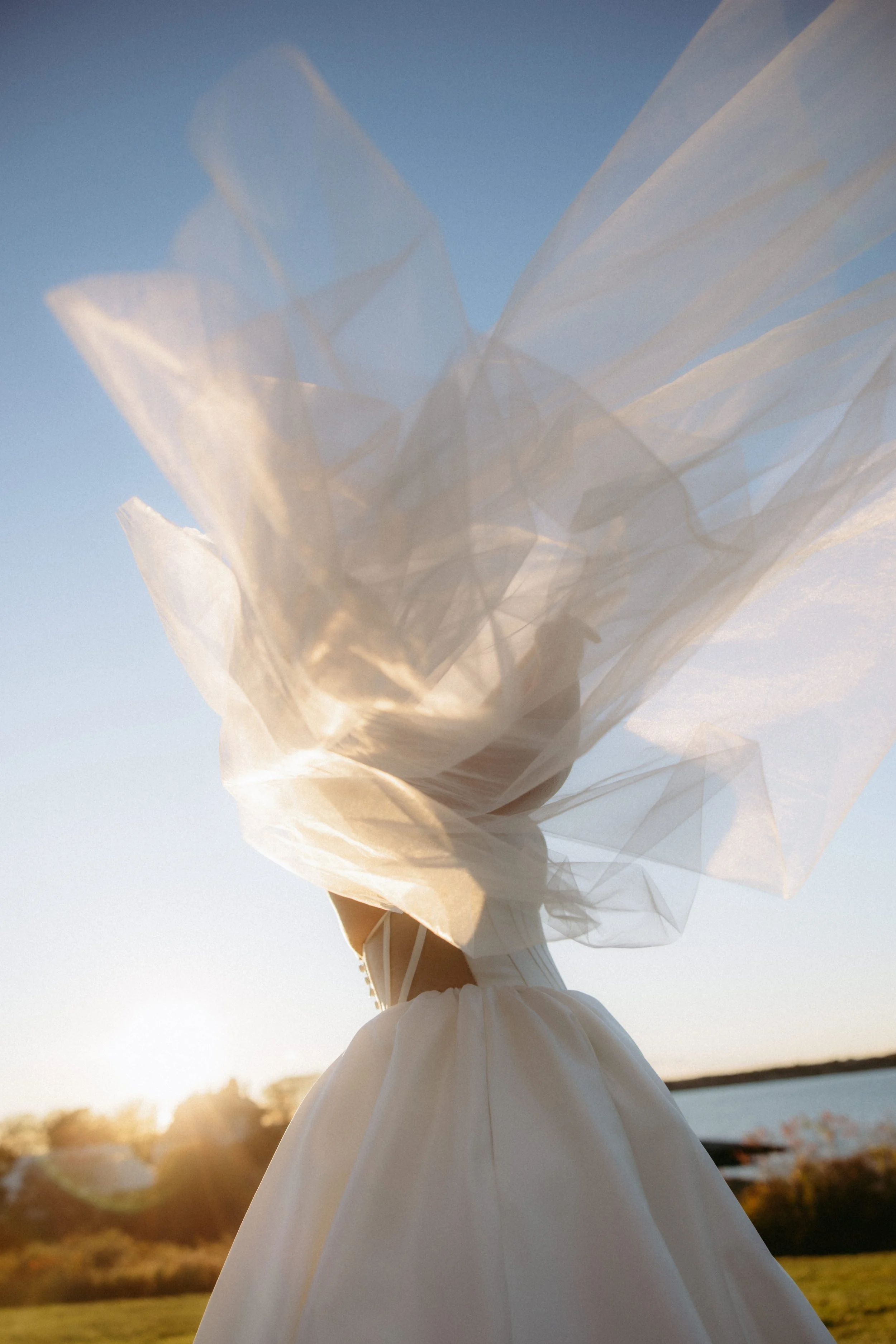 A person holding a white, semi-transparent umbrella against a blue sky with the sun setting, creating a warm glow.