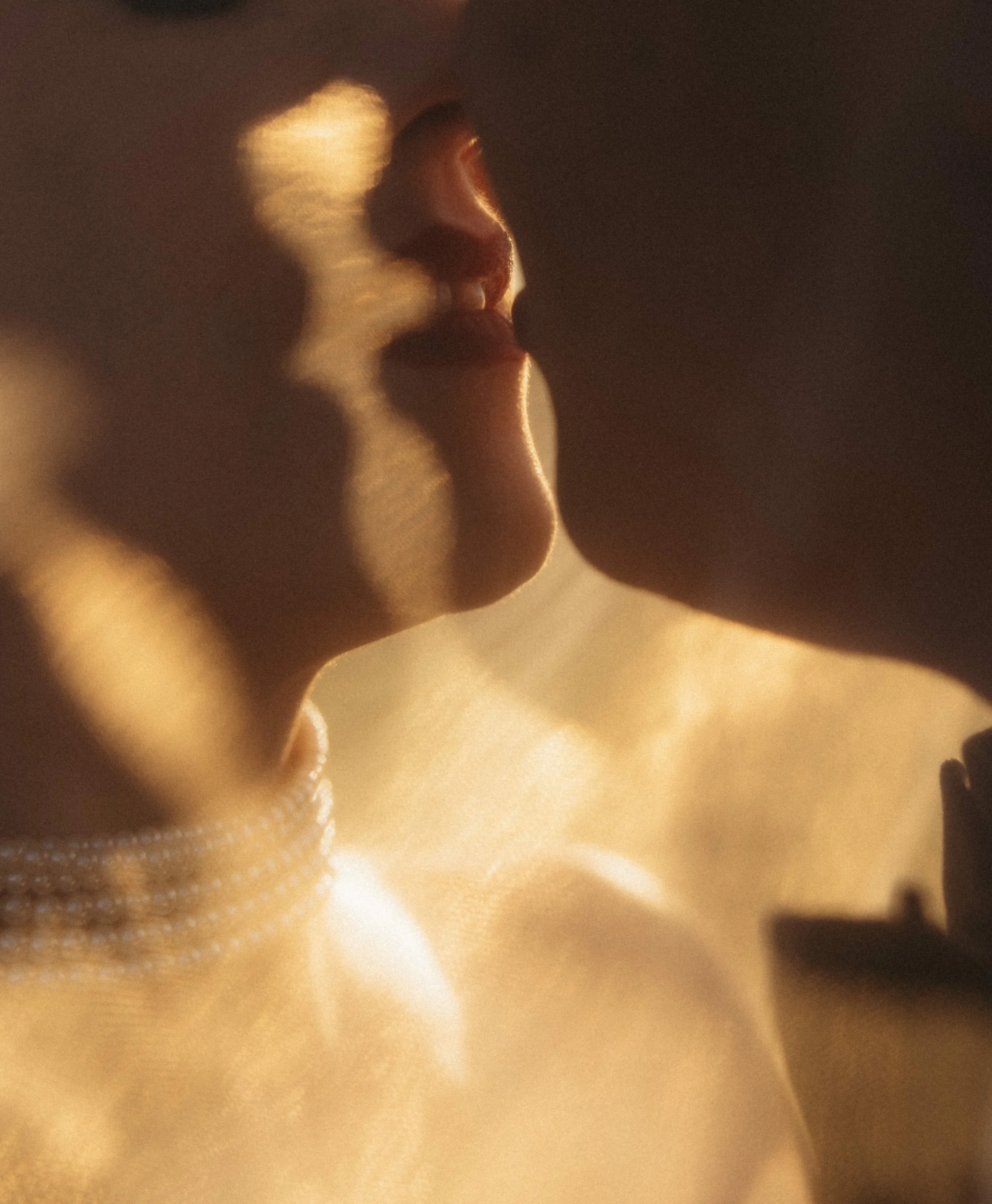 A close-up of a person's face with eyes closed, lips parted, and their hand touching their chin in a contemplative pose, warm lighting creating soft shadows.