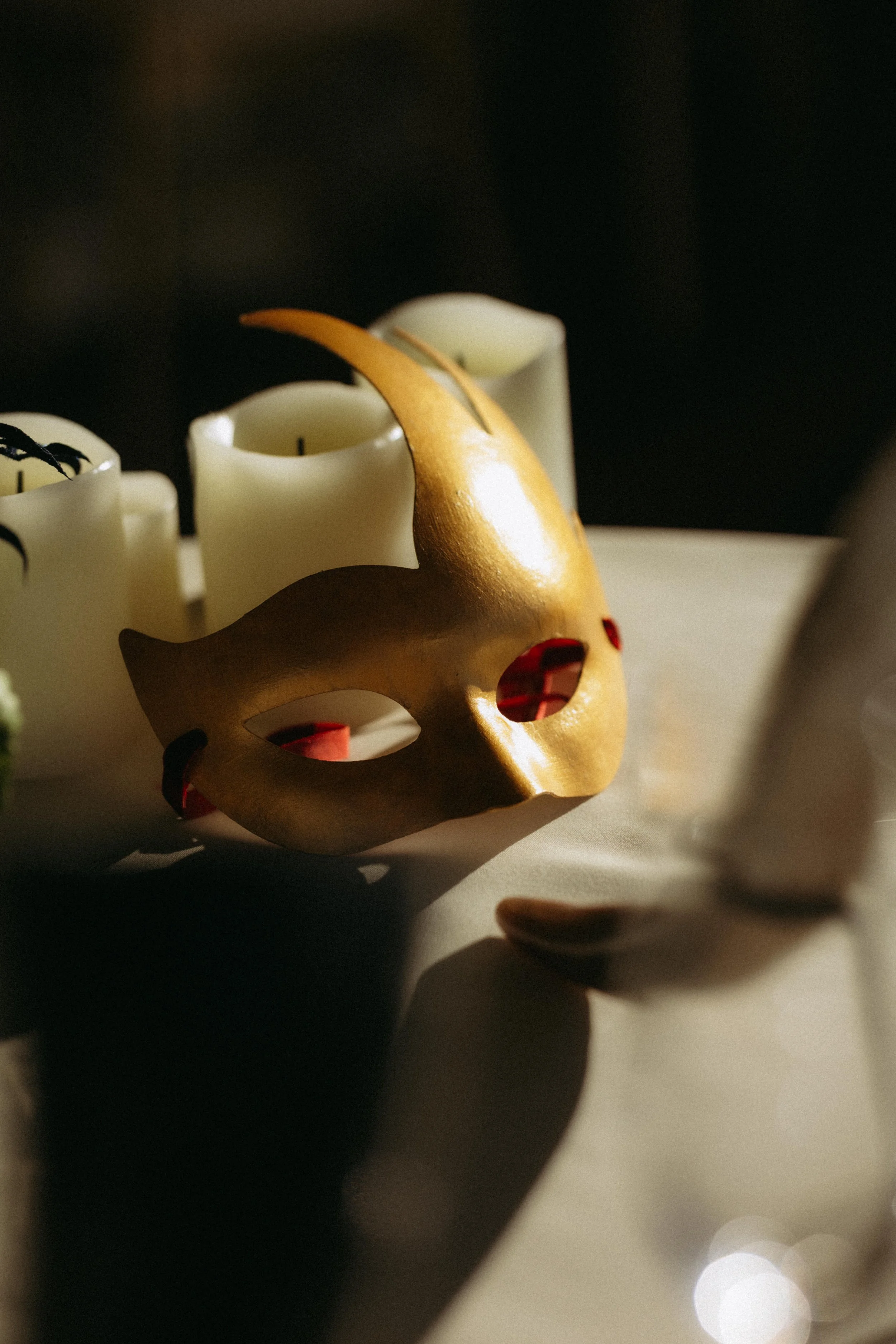 Close-up of a decorative gold skull with red eyes surrounded by white candles against a dark background.