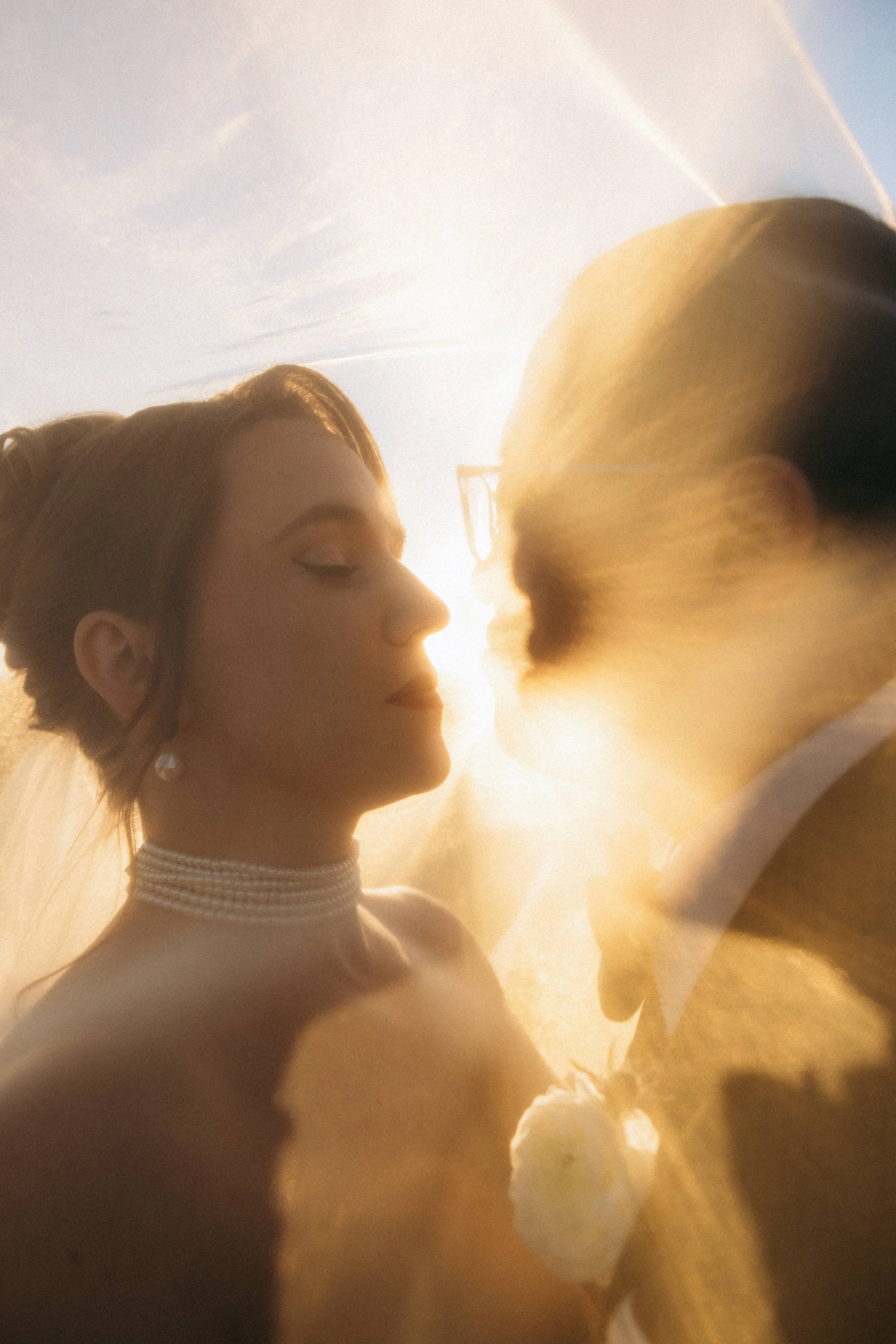 A close-up shot of a bride and groom sharing a kiss during their wedding, with warm sunlight illuminating them in the background.