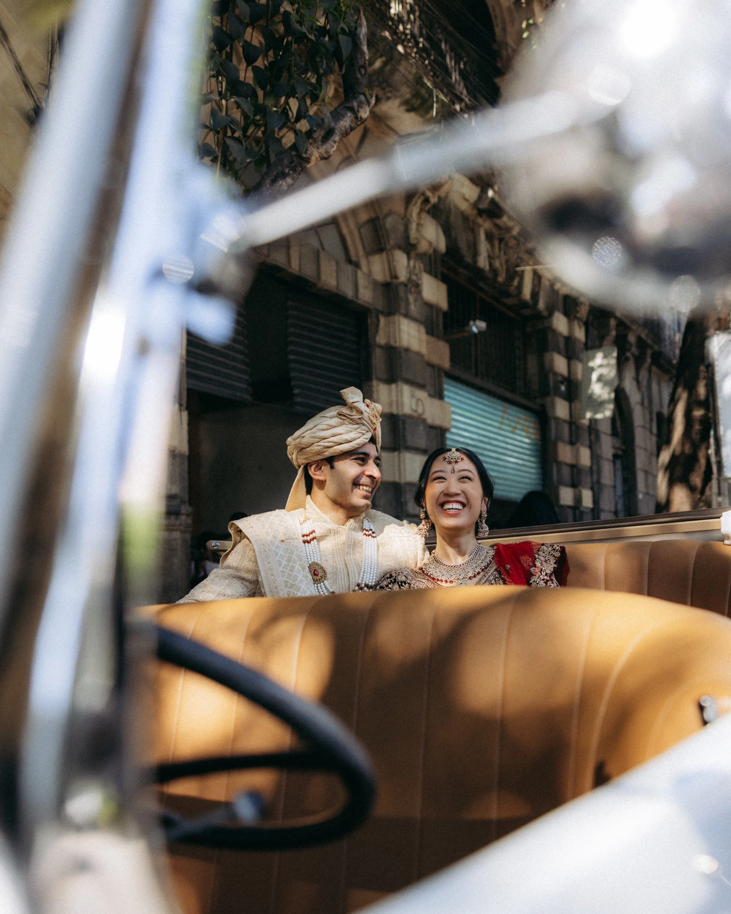 Two people wearing traditional South Asian attire are smiling and sitting close together, with their heads touching, in a setting that appears to be a restaurant or cafe. The image captures their joyful expressions.