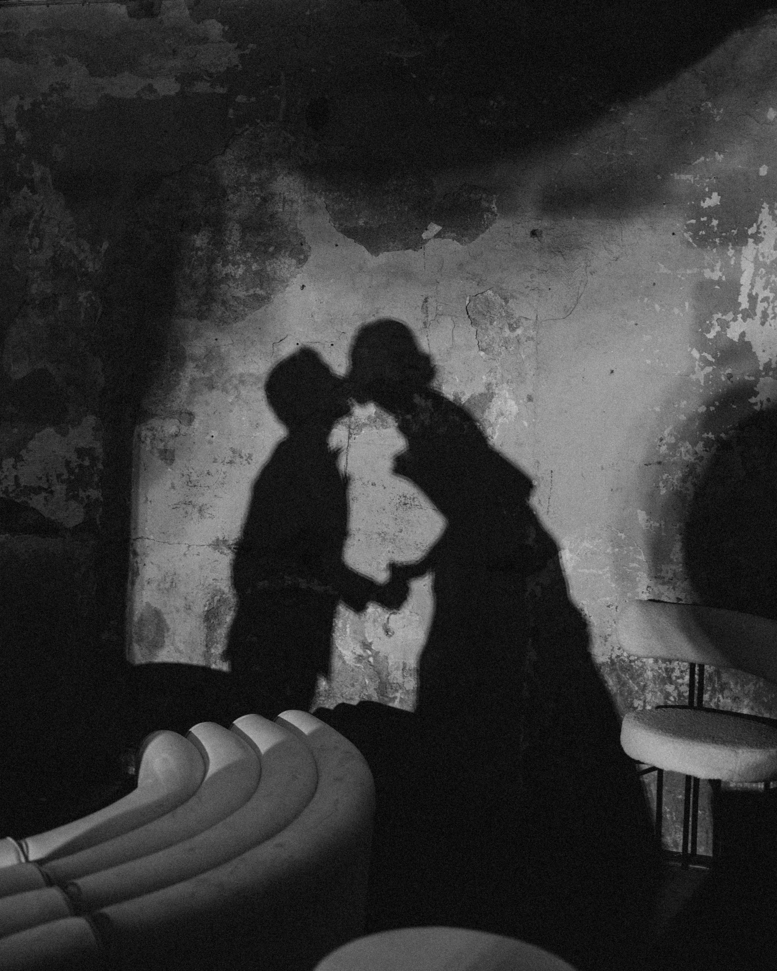 Shadows of two people holding hands with their arms raised, cast on a textured floor with debris and a railing in the foreground.